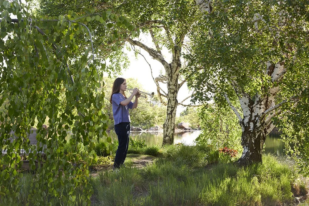 senior portrait of trumpet playing teen under trees by lake