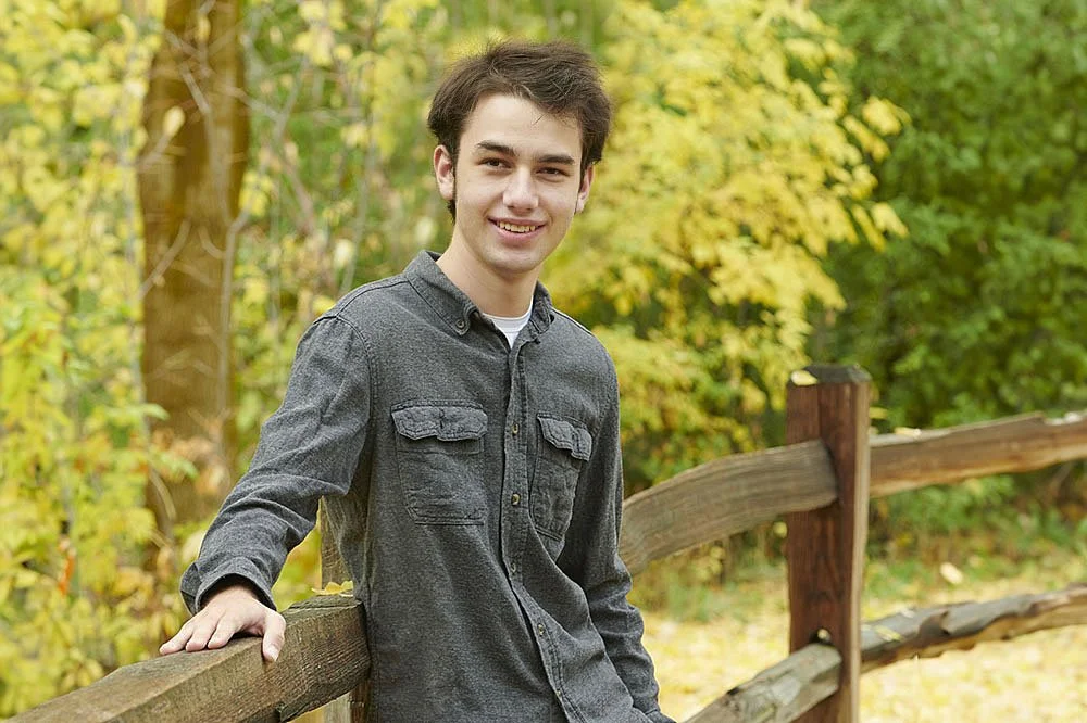 senior portrait of teen boy along wood fence in fall scene