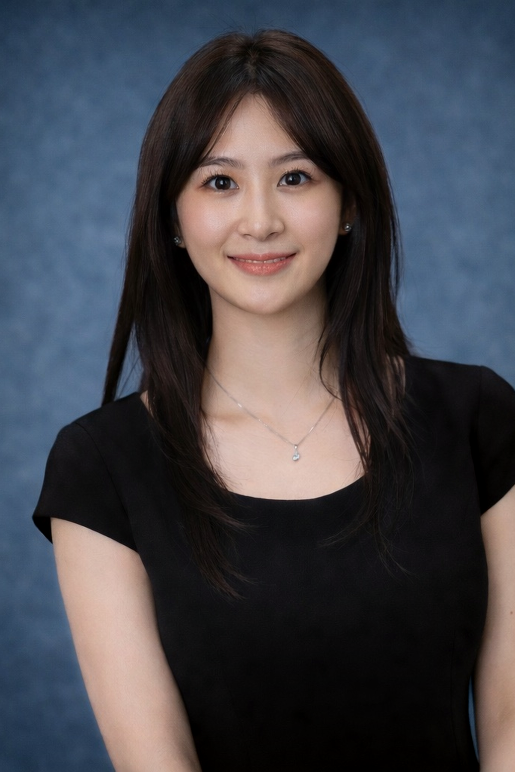 A woman with long dark hair wearing a black top and silver jewelry, smiling against a blue background.