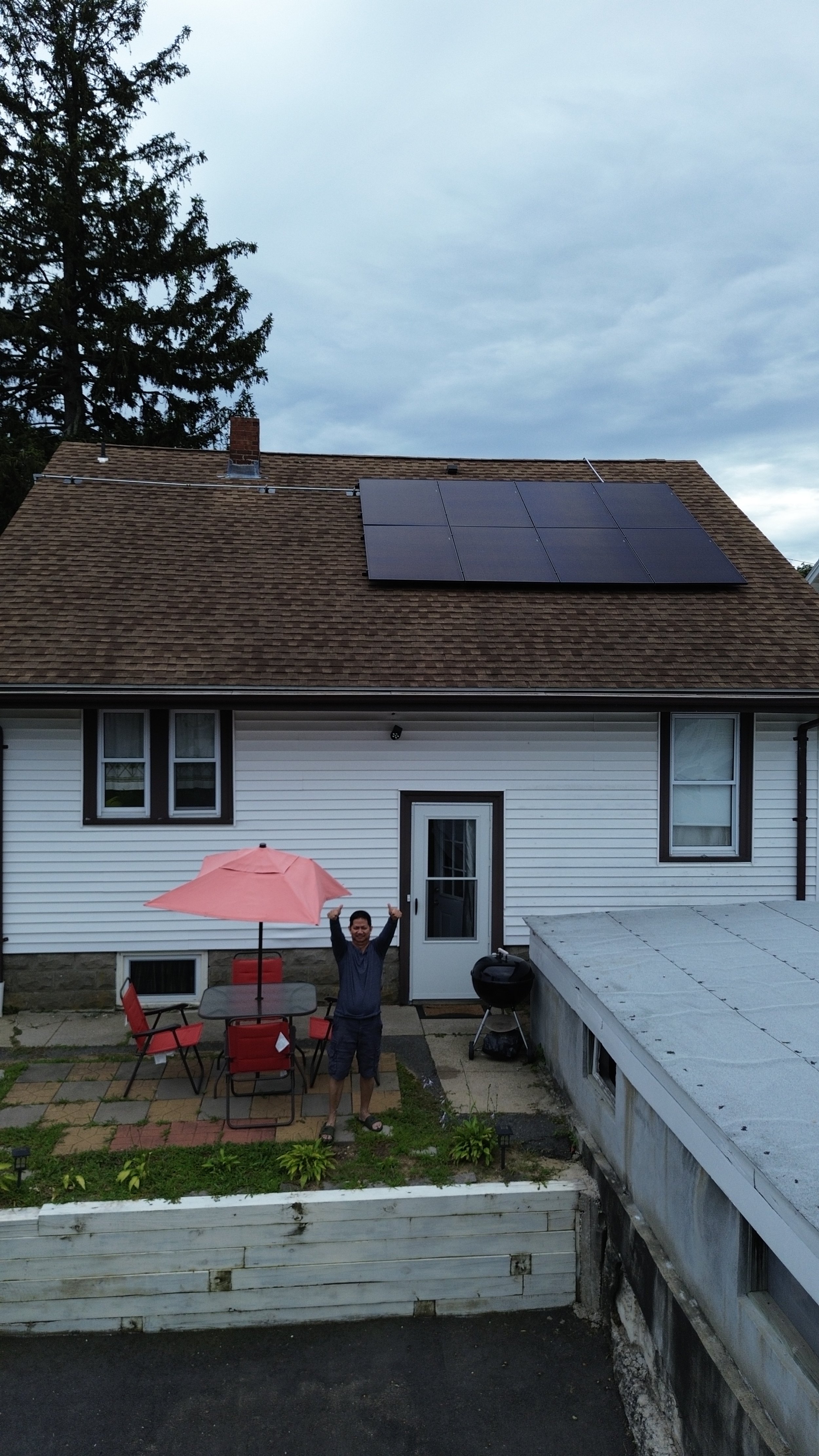 House with solar panels on roof, person standing outside, patio with umbrella