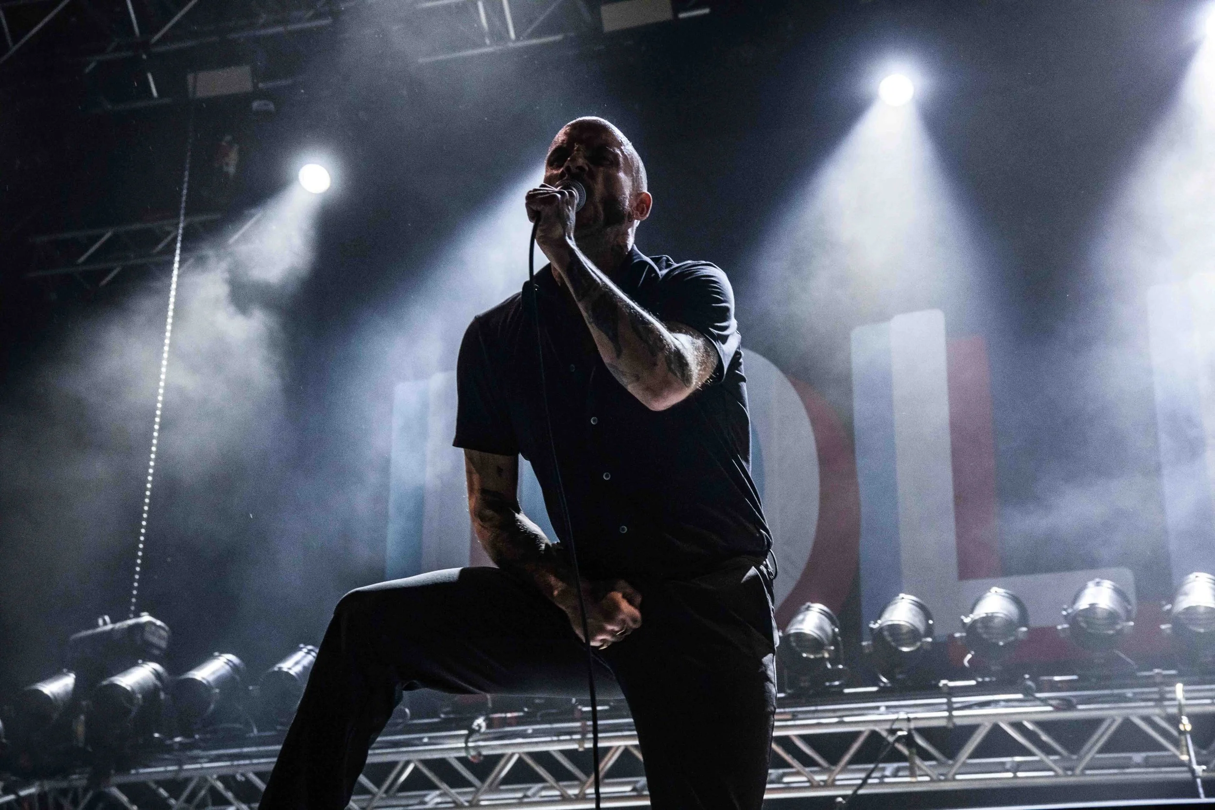 A male singer performing on stage with a microphone, with stage lights and smoke creating a dramatic atmosphere.