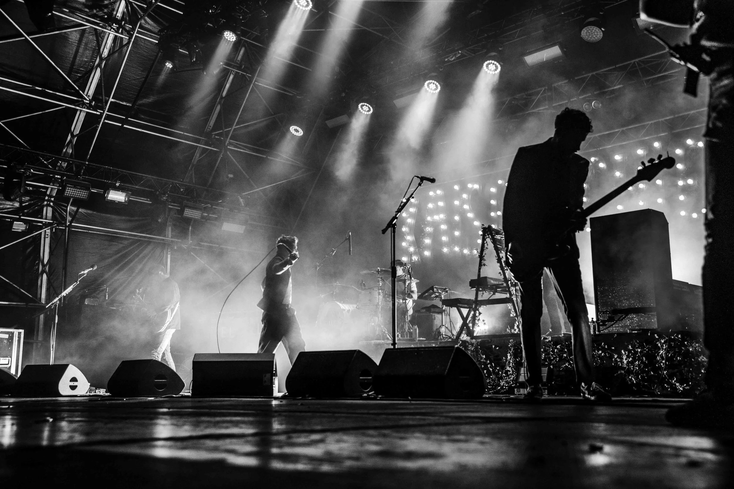 Silhouettes of band members performing on stage with bright lights and fog effects.