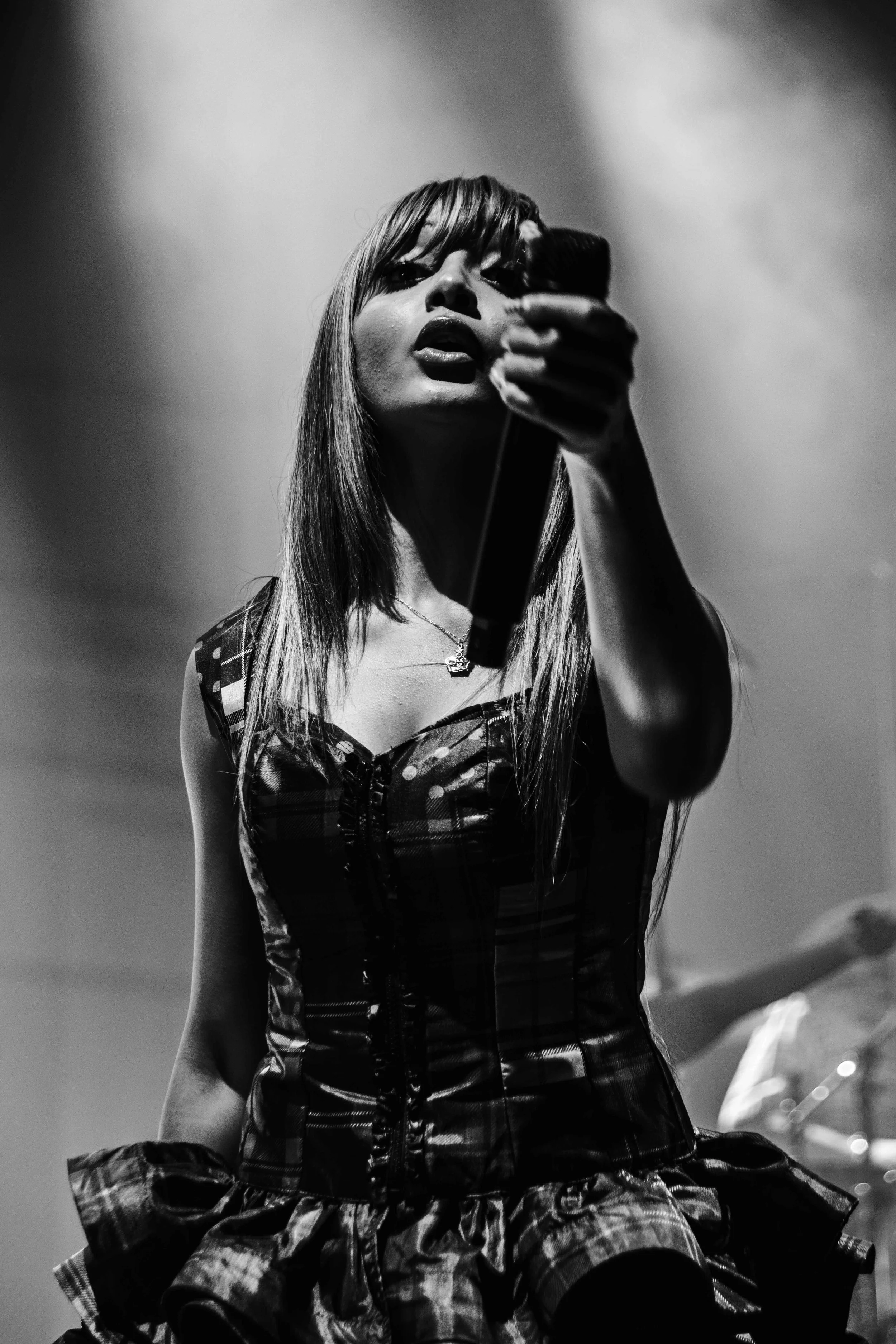 A black-and-white photo of a woman in a plaid dress taking a selfie with a mirror,-studio stage lighting in the background.