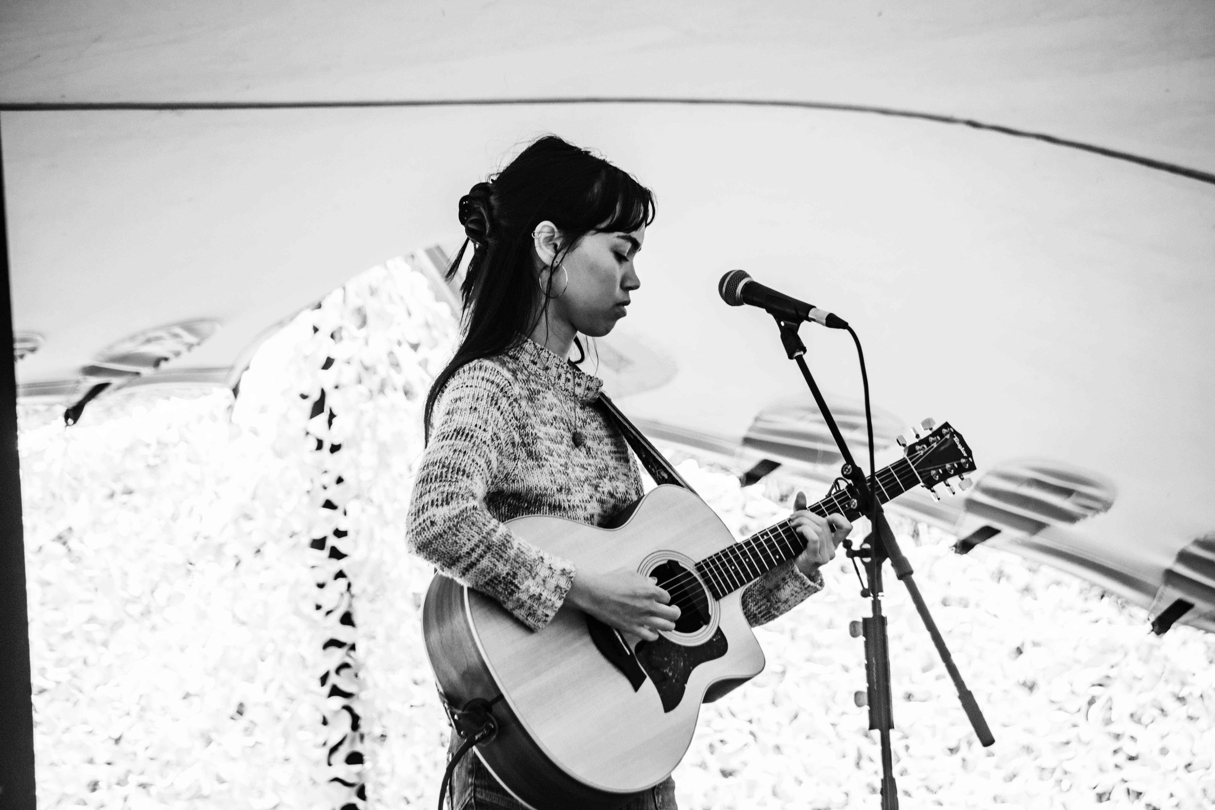 A woman playing an acoustic guitar and singing into a microphone on a stage.