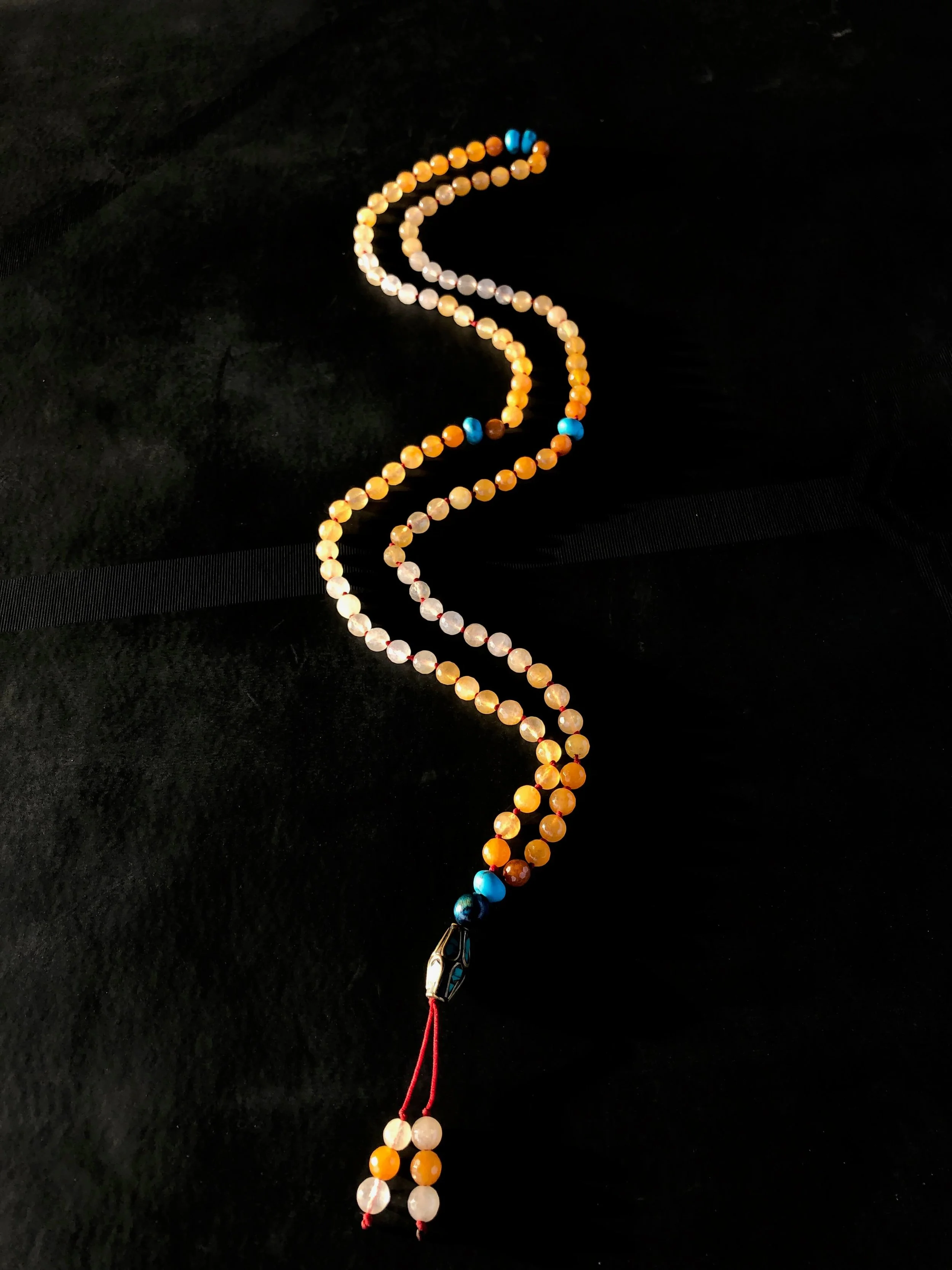 A beaded rosary with orange, white, light pink, and blue beads, laid out on a black fabric background.