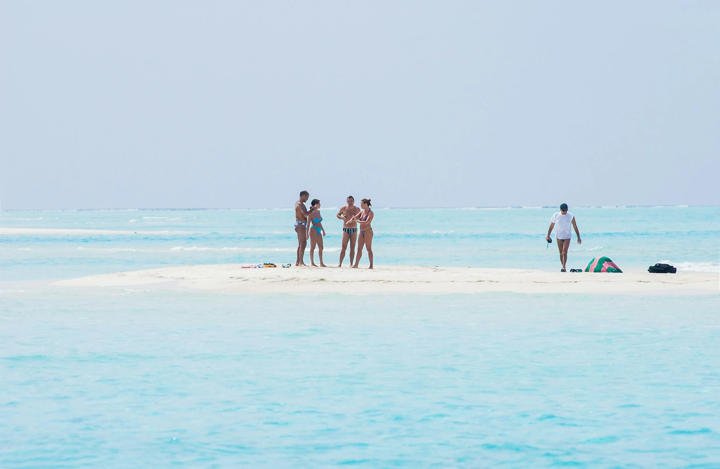 Group of travellers standing on a white sandbank in the Maldives’ shallow turquoise lagoon