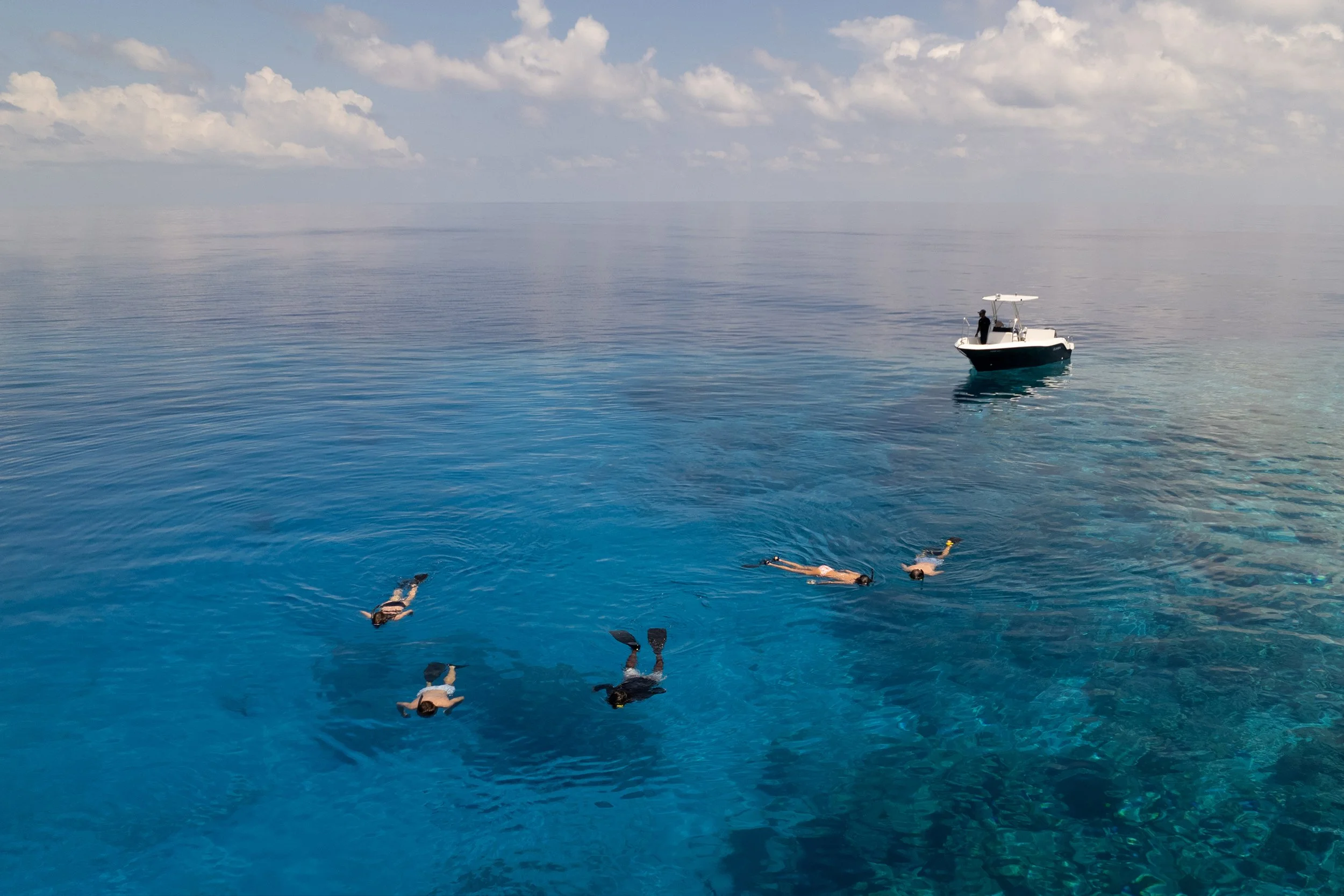 Group of snorkelers exploring calm deep-blue Maldivian waters near a boat