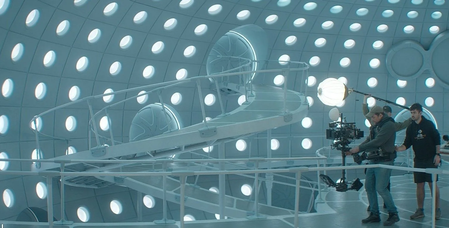 James Chesterton operating a professional film camera Arri Alexa 35 on set of Doctor Who with a futuristic, circular wall featuring evenly spaced illuminated portholes of the Tardis.
