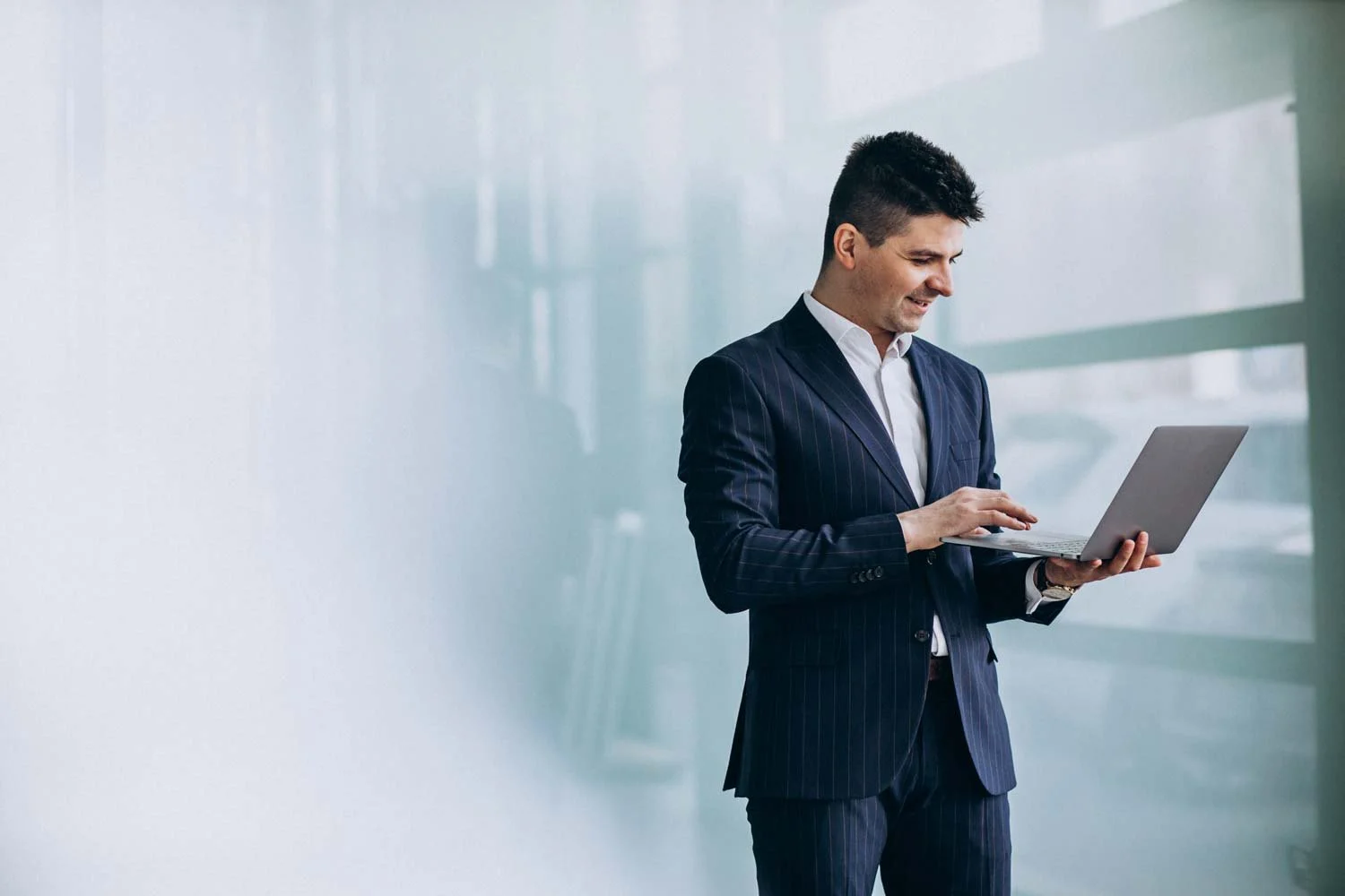 A man in a suit stands in front of a laptop, appearing focused and engaged in a professional setting.