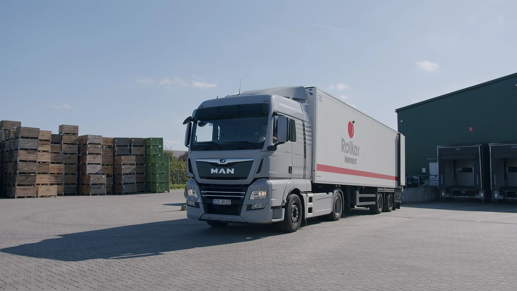 Ein MAN-LKW steht auf einem gepflasterten Platz neben Paletten und einem Gebäudeteil.