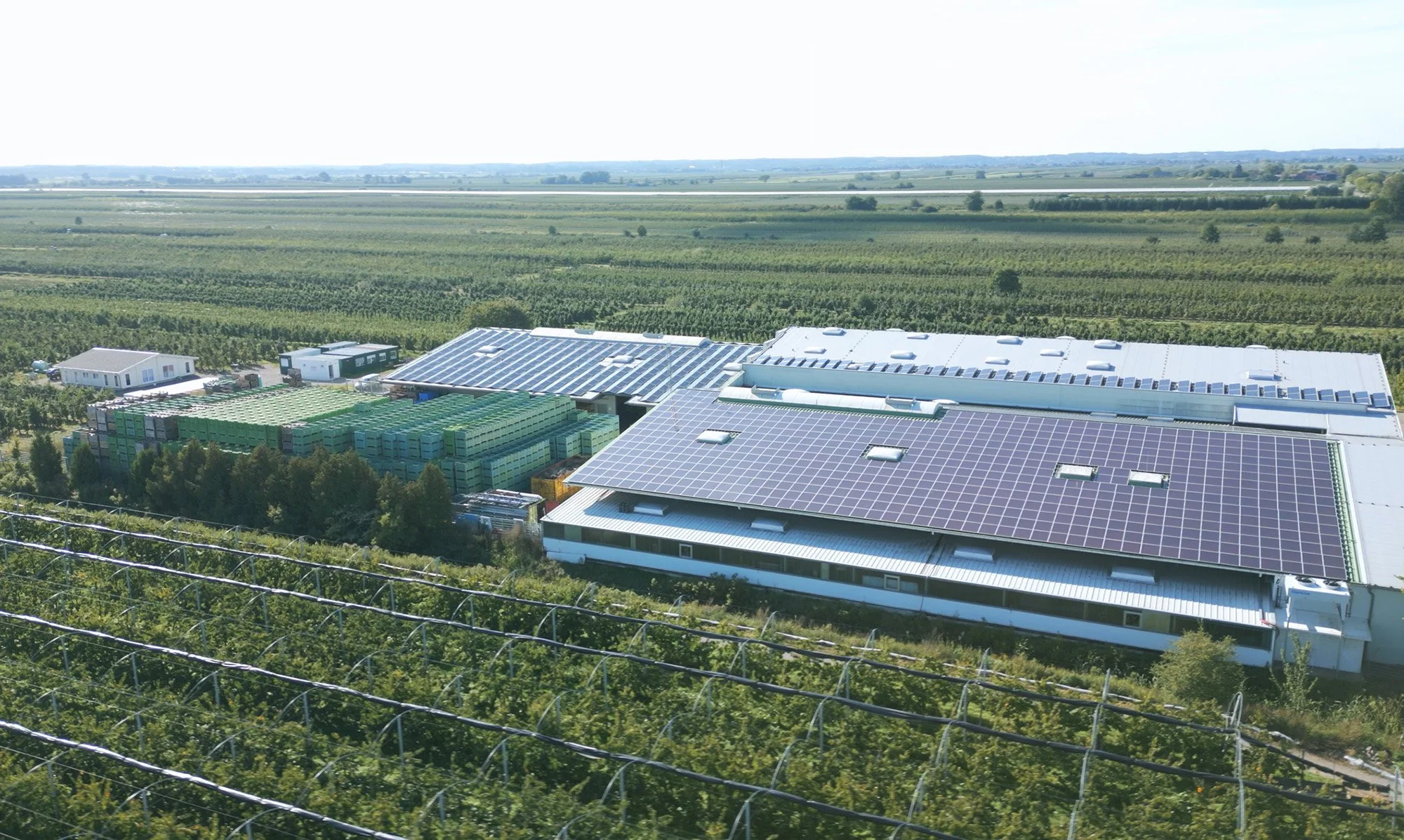 Luftaufnahme eines Gebäudes mit Solarpanelen auf dem Dach, umgeben von landwirtschaftlicher Fläche und Feldern.