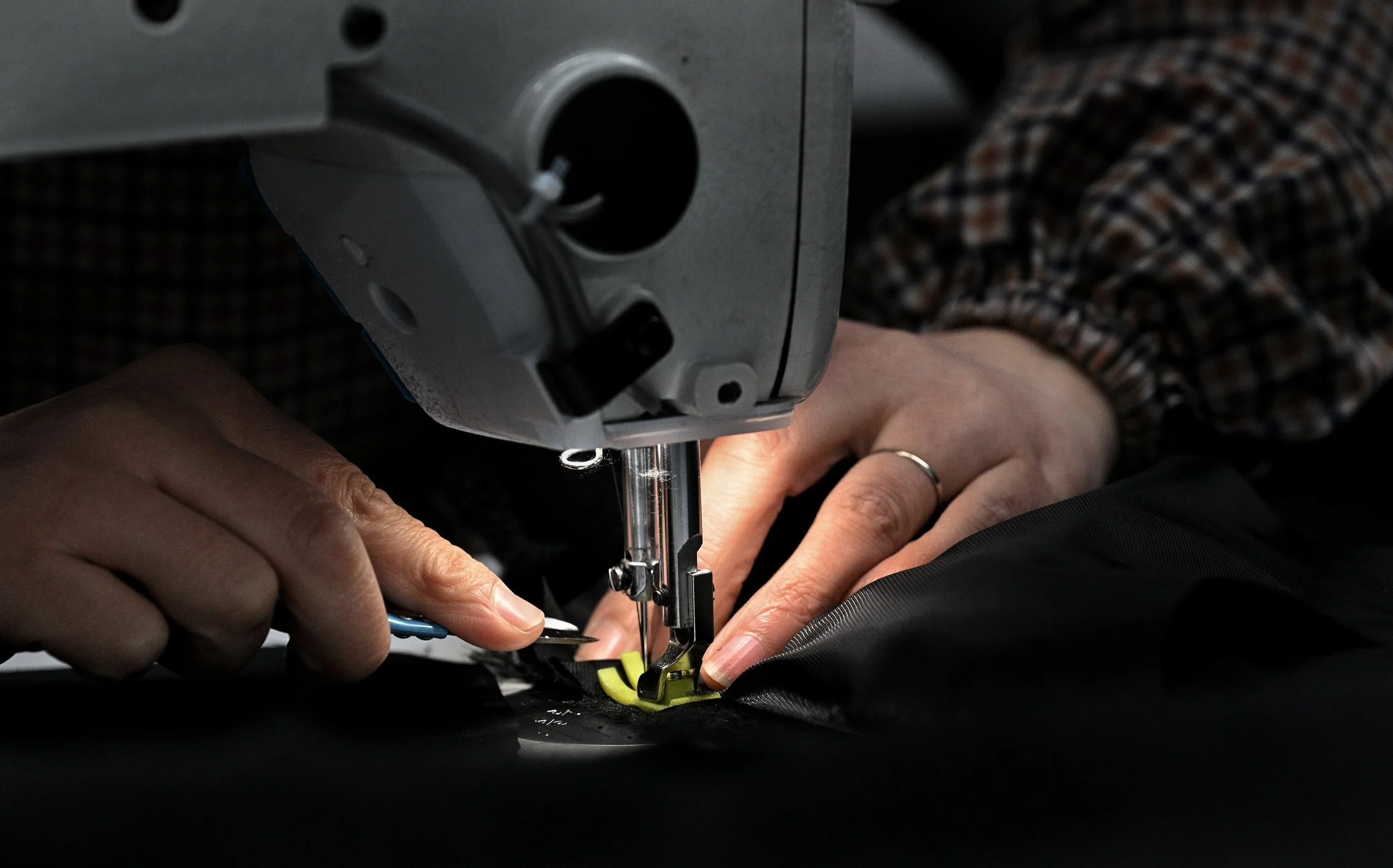 Close-up of hands guiding fabric through a sewing machine, with a person wearing a checkered shirt working on sewing or quilting.