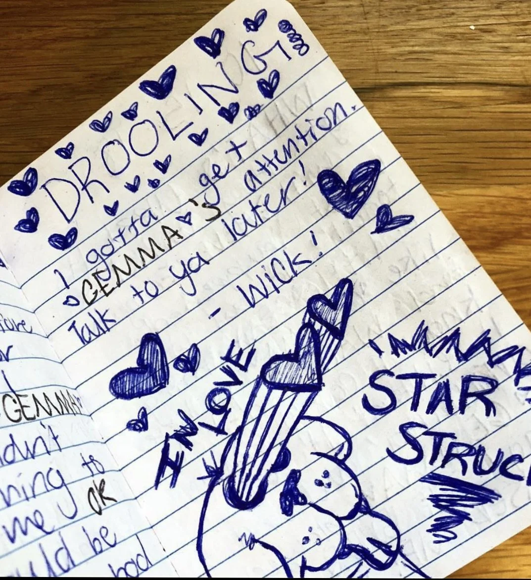 Notebook page with blue ink doodles and text, including hearts and phrases like "DROOLING," "IN LOVE," and "STAR STRUCK."