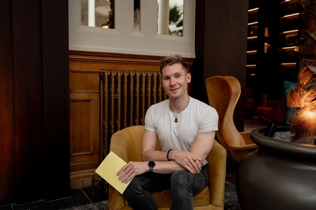Liam Marshall, content writer and copywriter, sitting in a mustard armchair holding a notebook in a relaxed workspace.