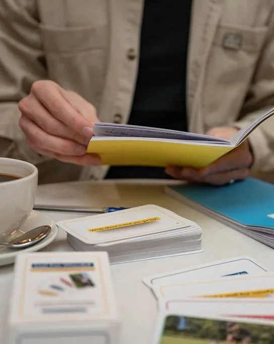 Creative writing prompt cards on a table beside a notebook, pen and coffee cup, being used for quiet writing time