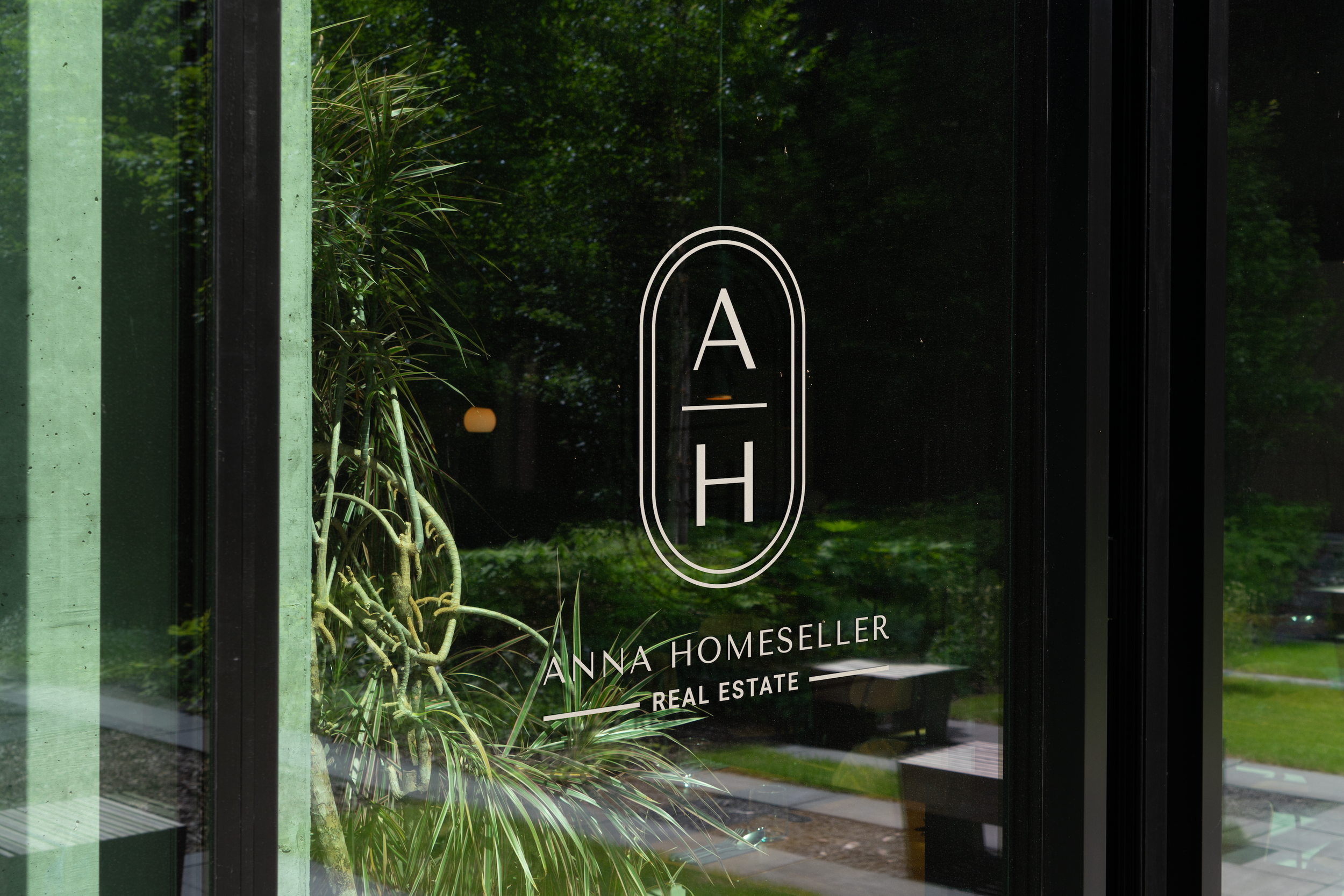 Glass door with The Anna monogram logo and greenery reflection.