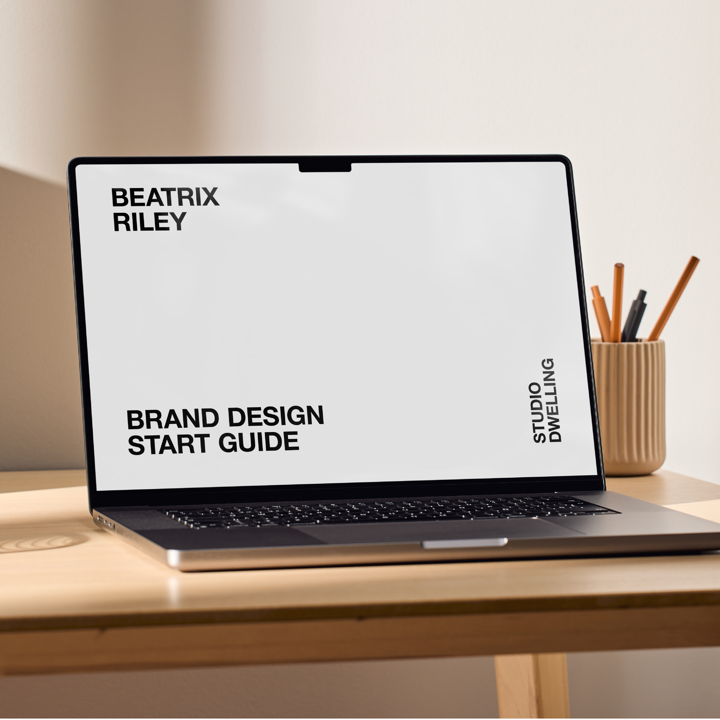 Laptop displaying "Brand Design Start Guide" on a wooden desk with a pencil holder in the background.