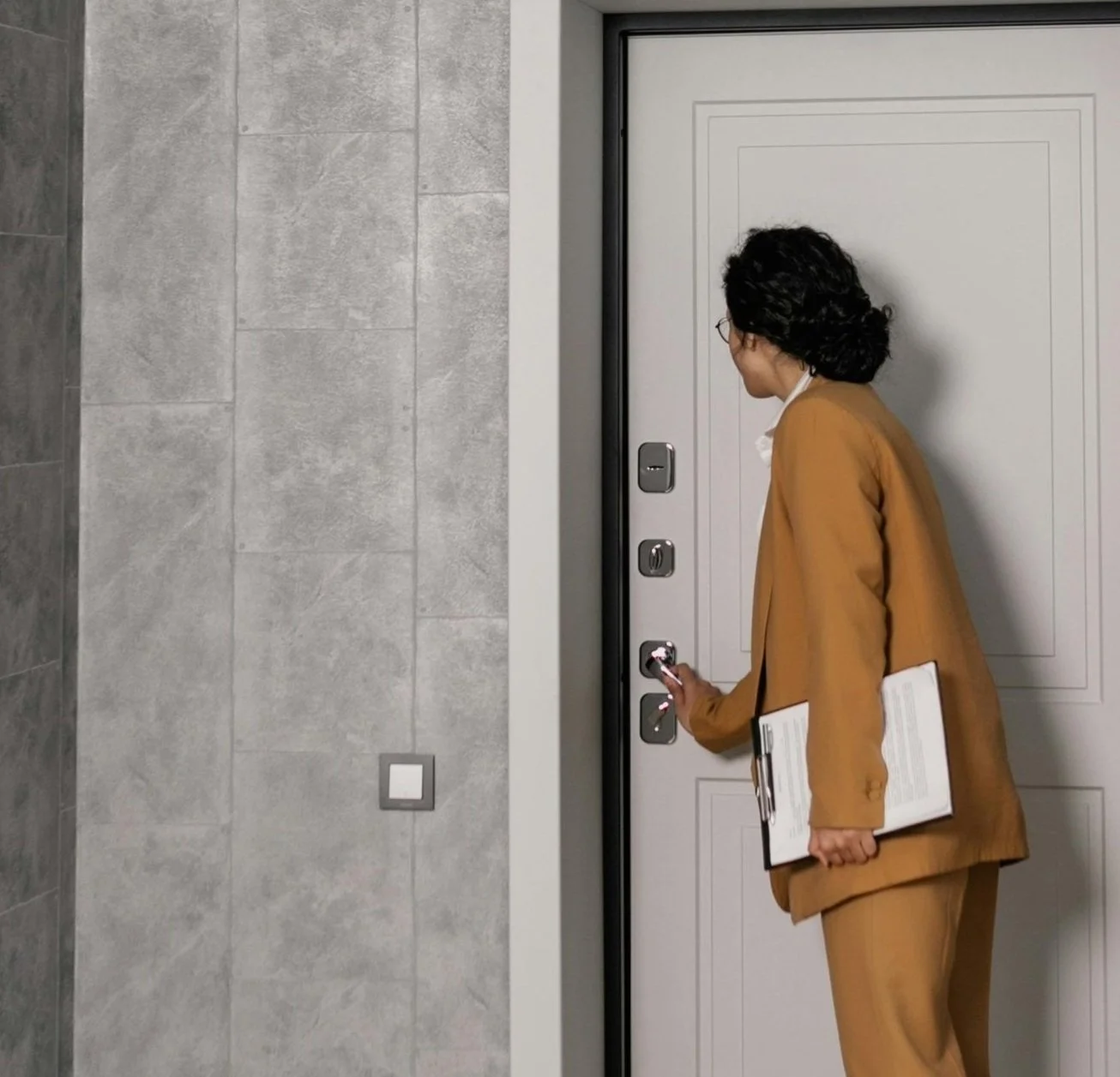 A real estate agent in a brown suite holding papers opening the door to an apartment.
