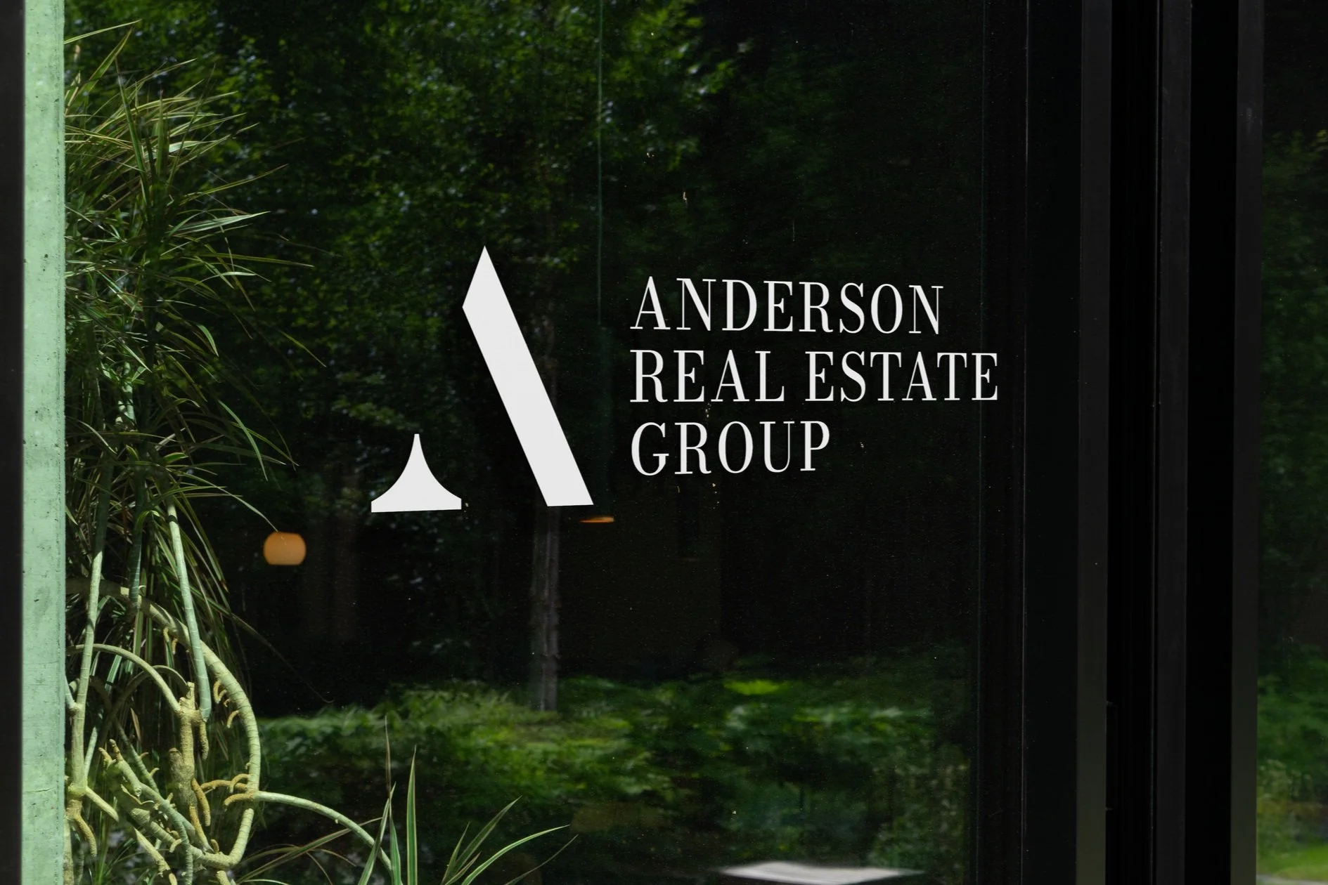 Logo of Anderson Real Estate Group on a glass door with a plant in the reflection.