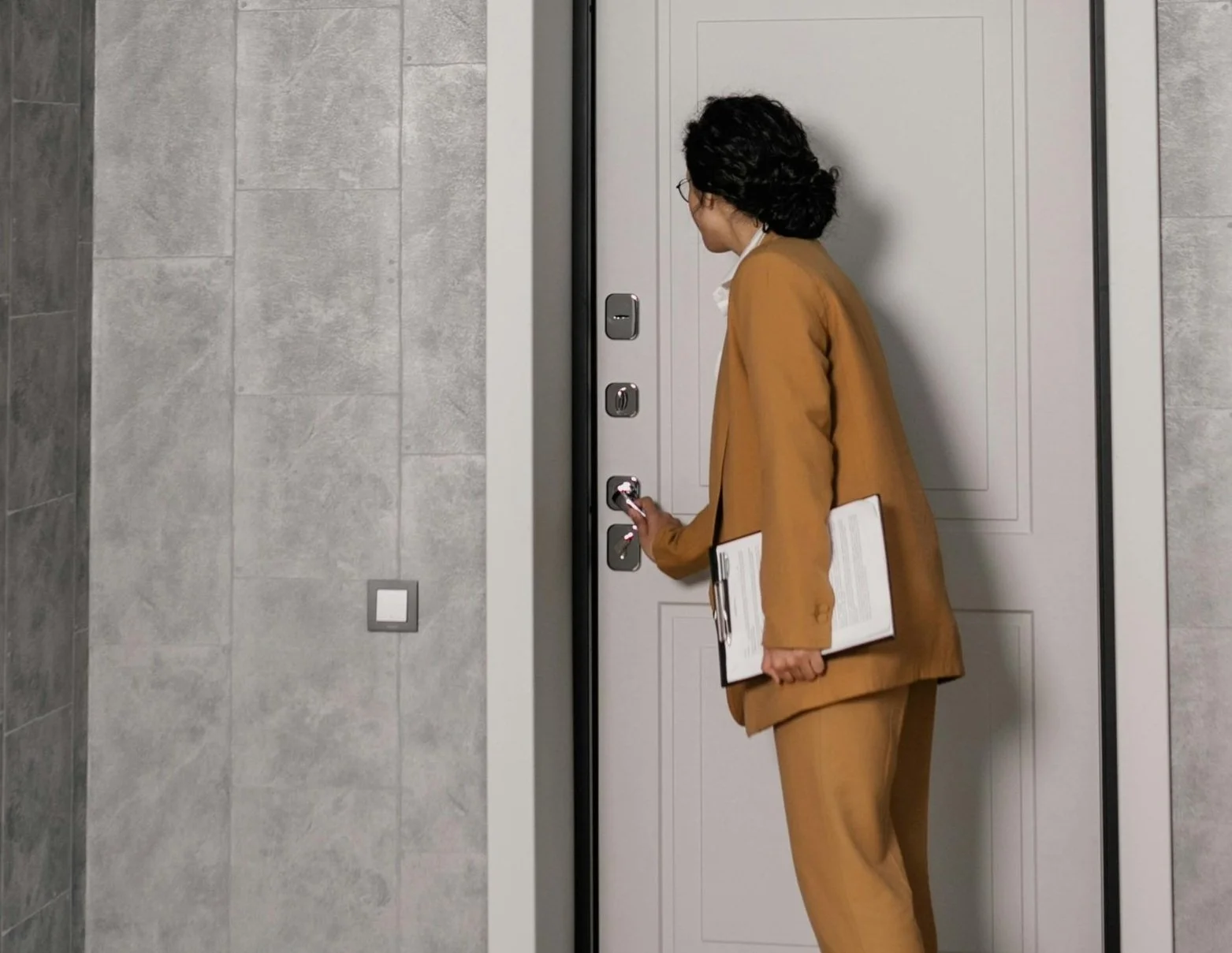 A real estate agent in a brown suite holding papers opening the door to an apartment.