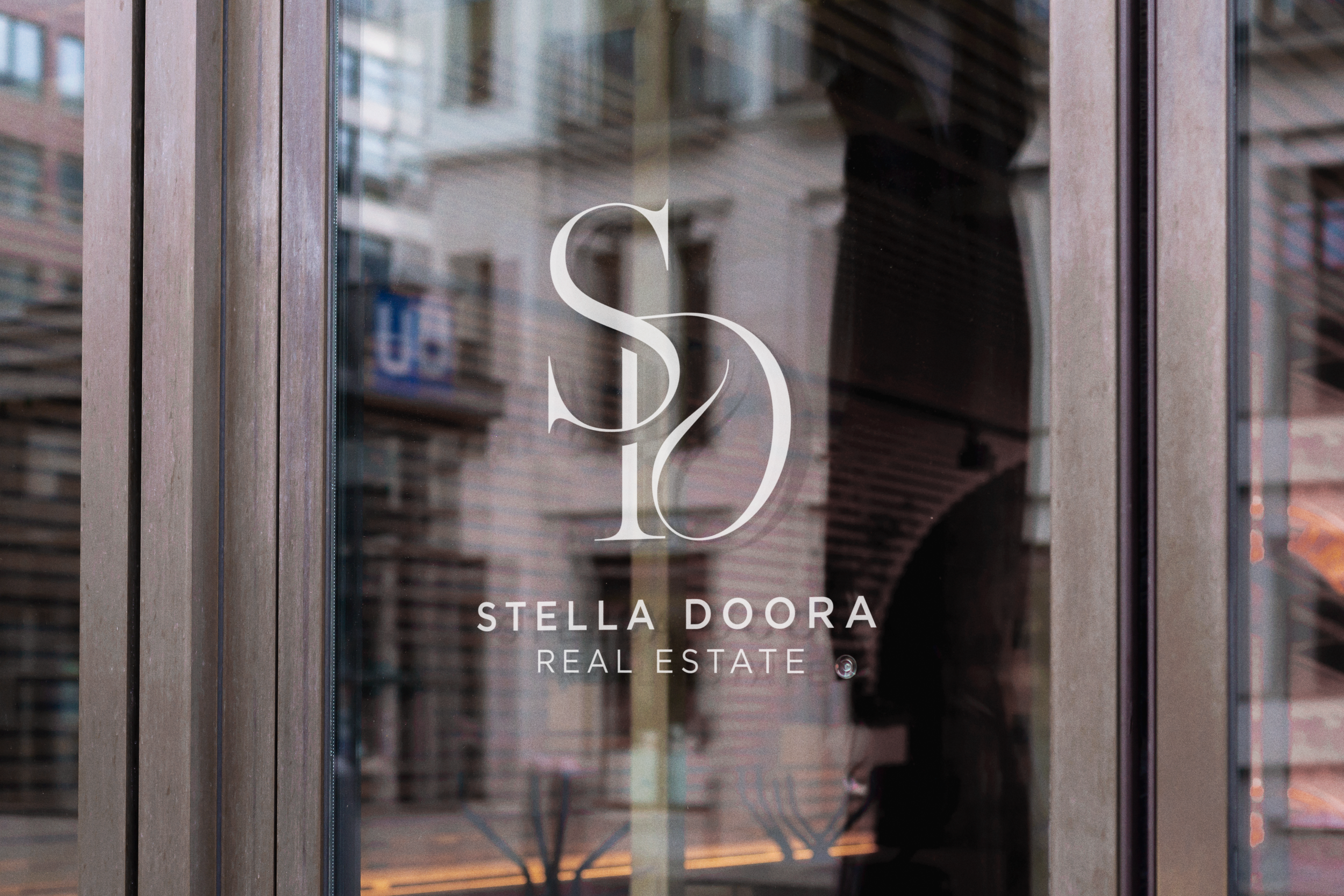 Glass window with The Stella monogram logo and building reflection.