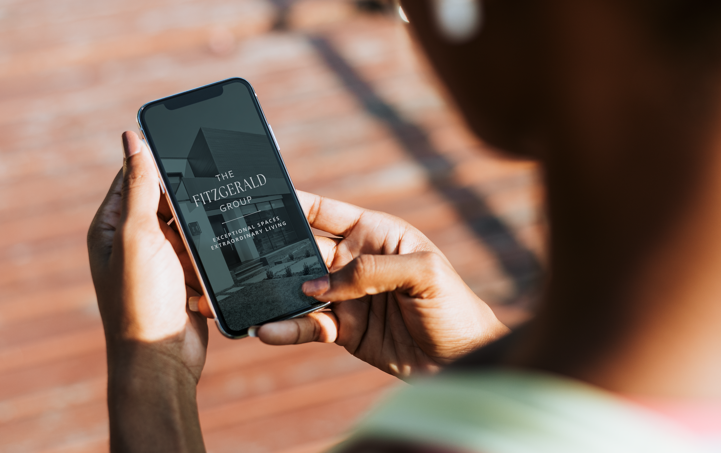 Person holding smartphone displaying "The Fitzgerald Group: Exceptional Spaces, Extraordinary Living."