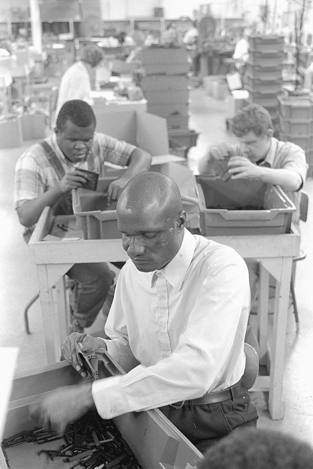 Workers assembling products in a factory setting, with boxes and trays on tables.