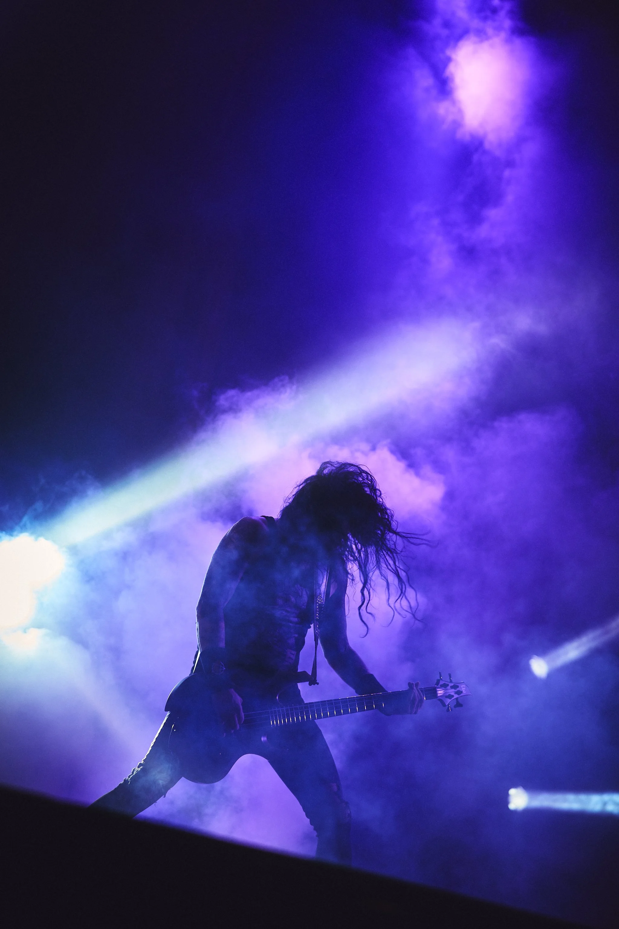Mies soittaa kitaraa savun ja violetin valaistuksen keskellä keikalla.