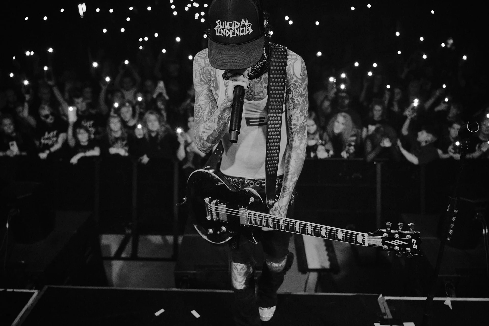 Mies esiintymässä kitaran kanssa lavalla, taustalla yleisö nostaa valoja ylös.