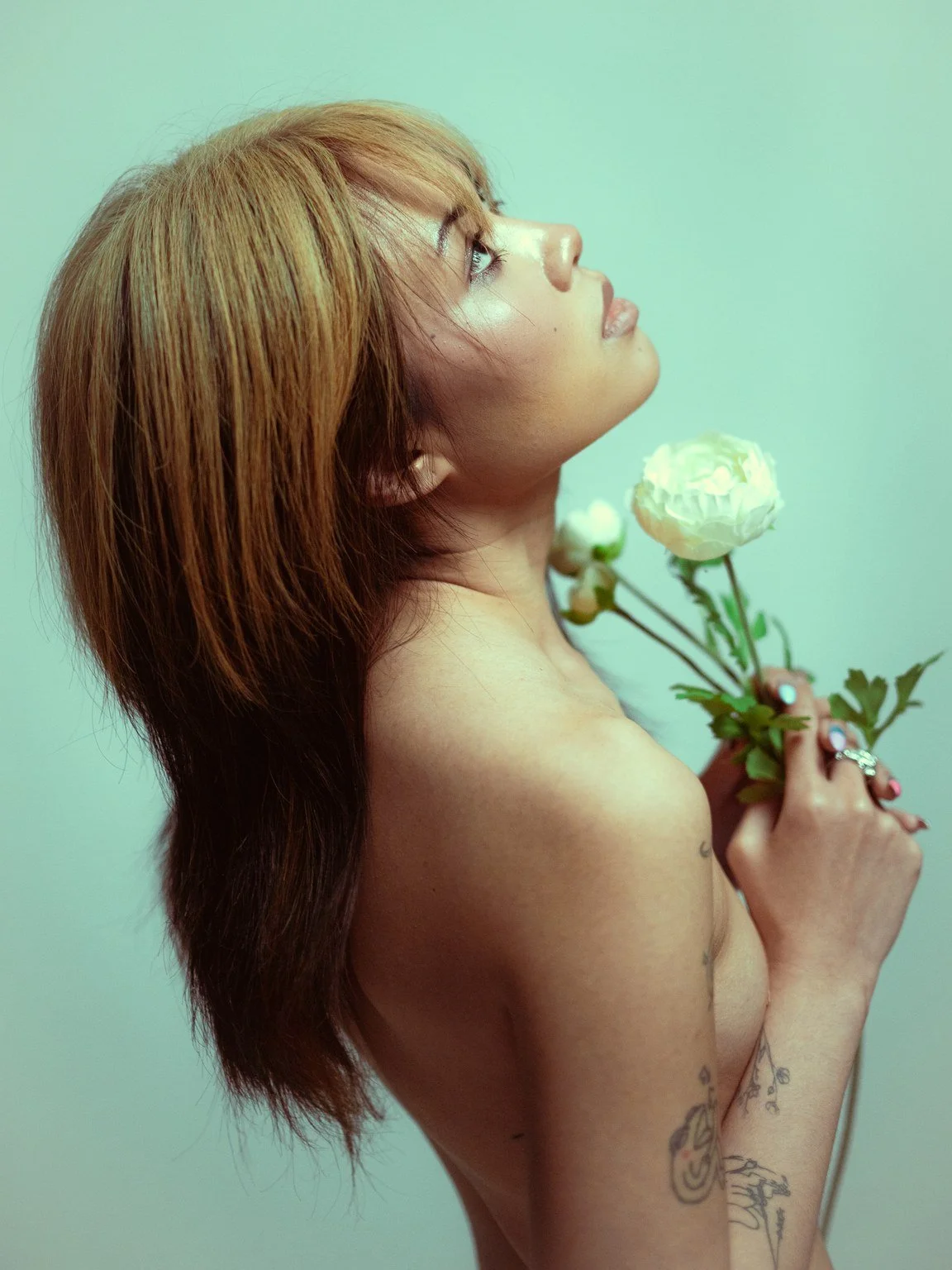 Nainen, jolla on ruskeat hiukset, katsoo ylös ja pitää valkoista kukkaa kädessään.