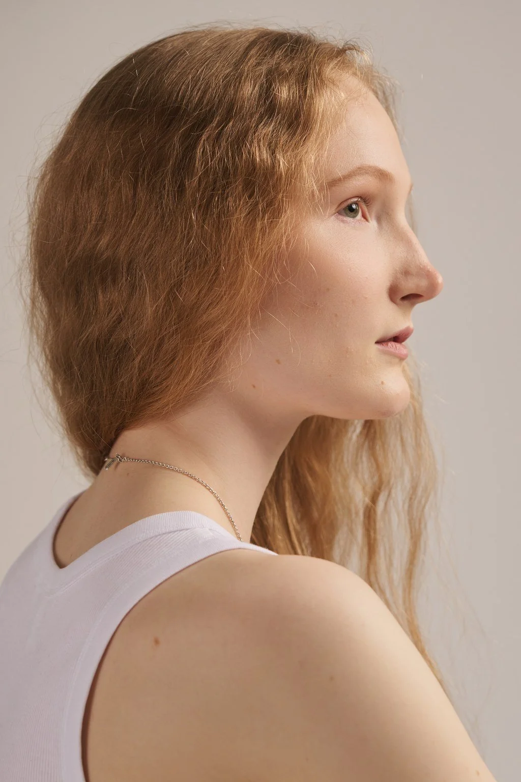 Samassa kuvassa oleva nuorten naisen profiilikuva, jolla on punaiset, kiharat hiukset ja vaalea iho, pukeutuneena valkoiseen toppiin ja hopeiseen ketjuun