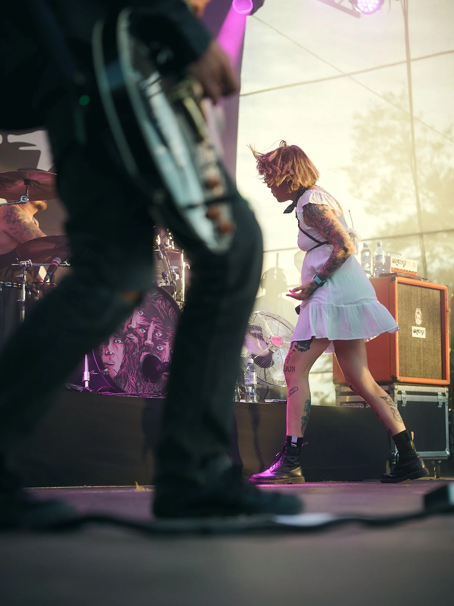 Esiintyjä musiikkifestivaalilla, taustalla rumpali, kitaristi etualalla. Lavalla valot ja musiikkilaitteistoa.