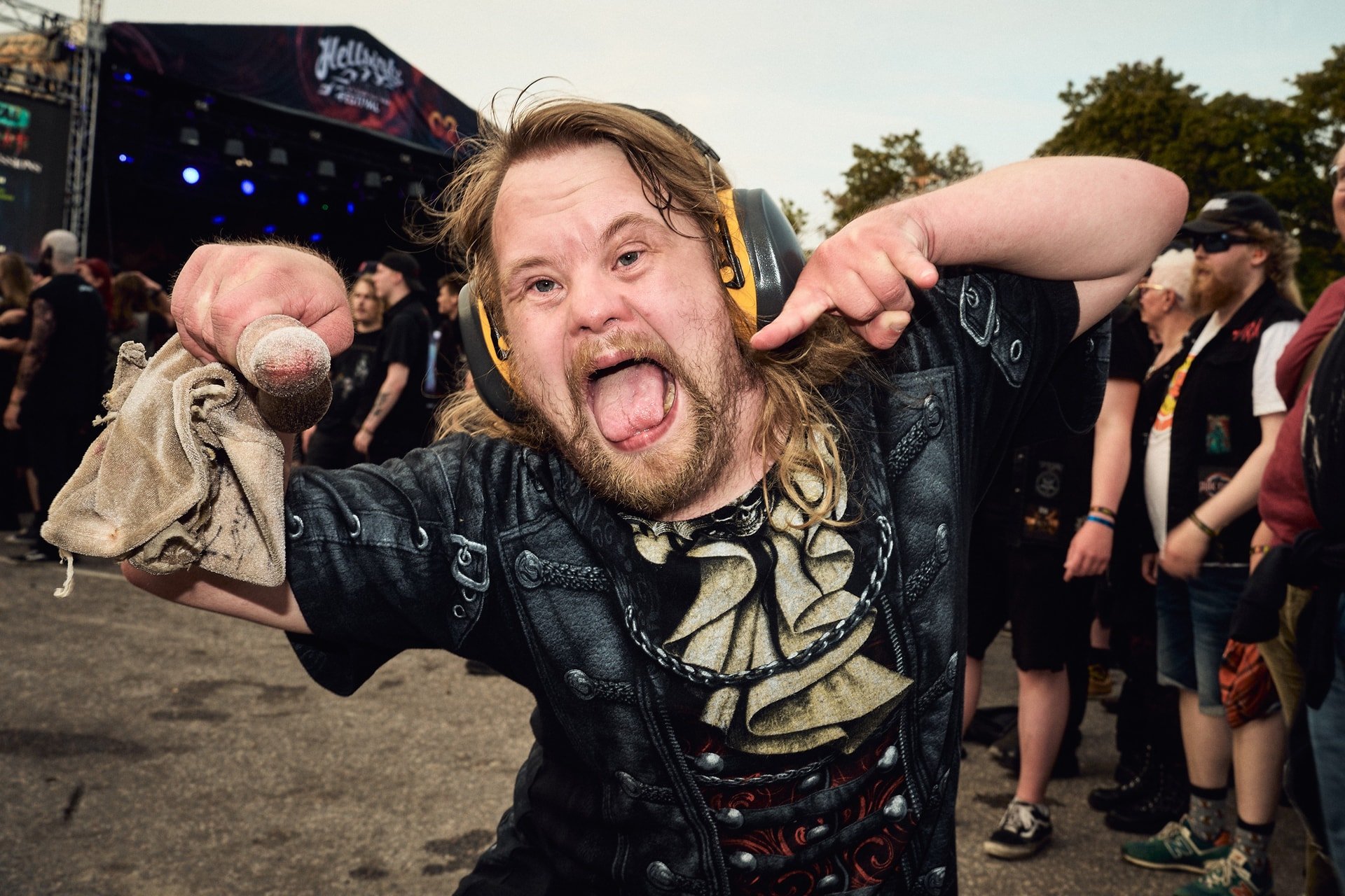 Mies kuuntelee musiikkifestivaaleilla kuulokkeet päässä, näyttää innokkaalta ja osoittaa itseään, taustalla on yleisöä ja lava.