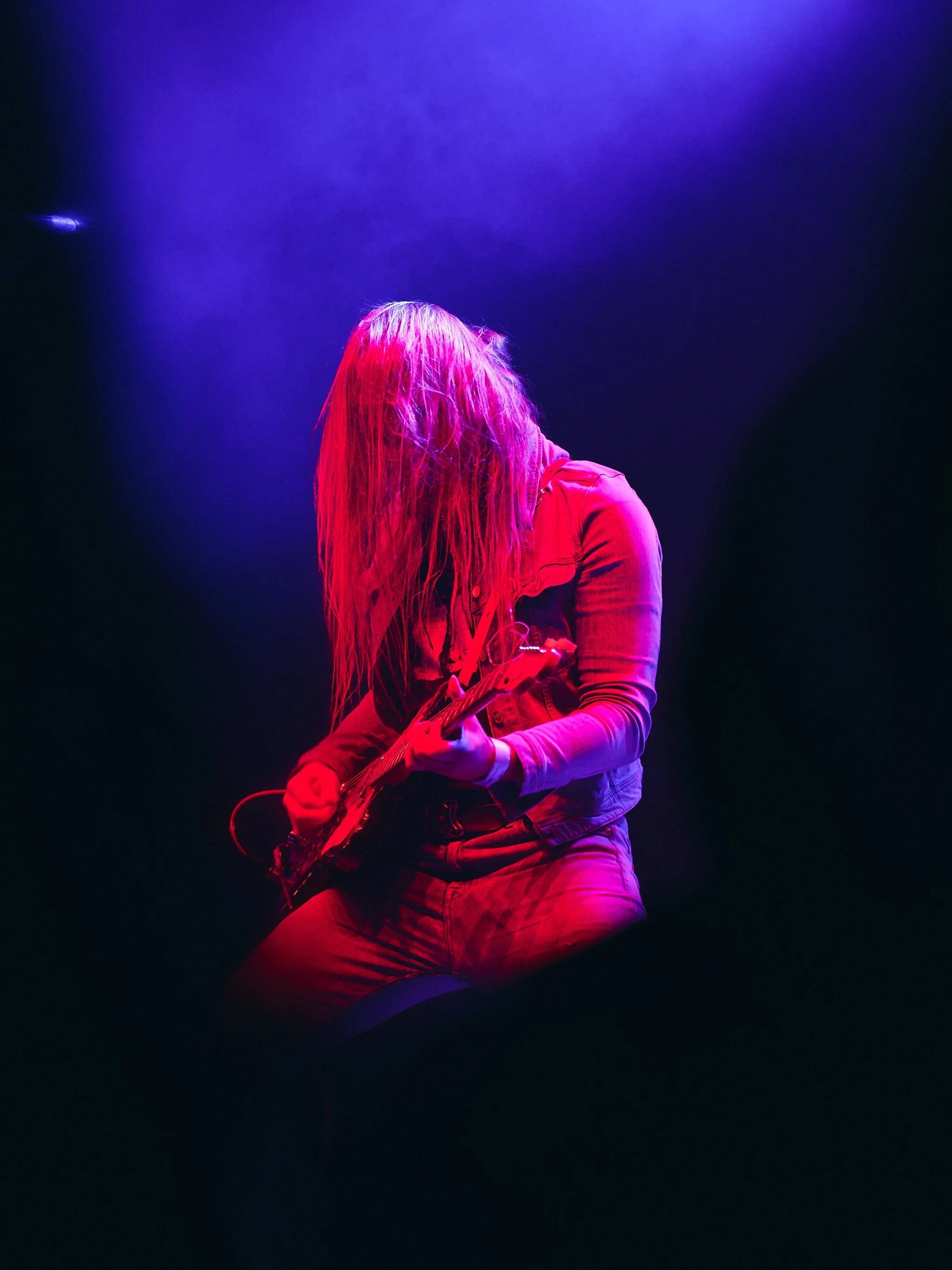 Kitaristi soittaa lavalla voimakkaassa punaisessa ja sinisessä valossa.