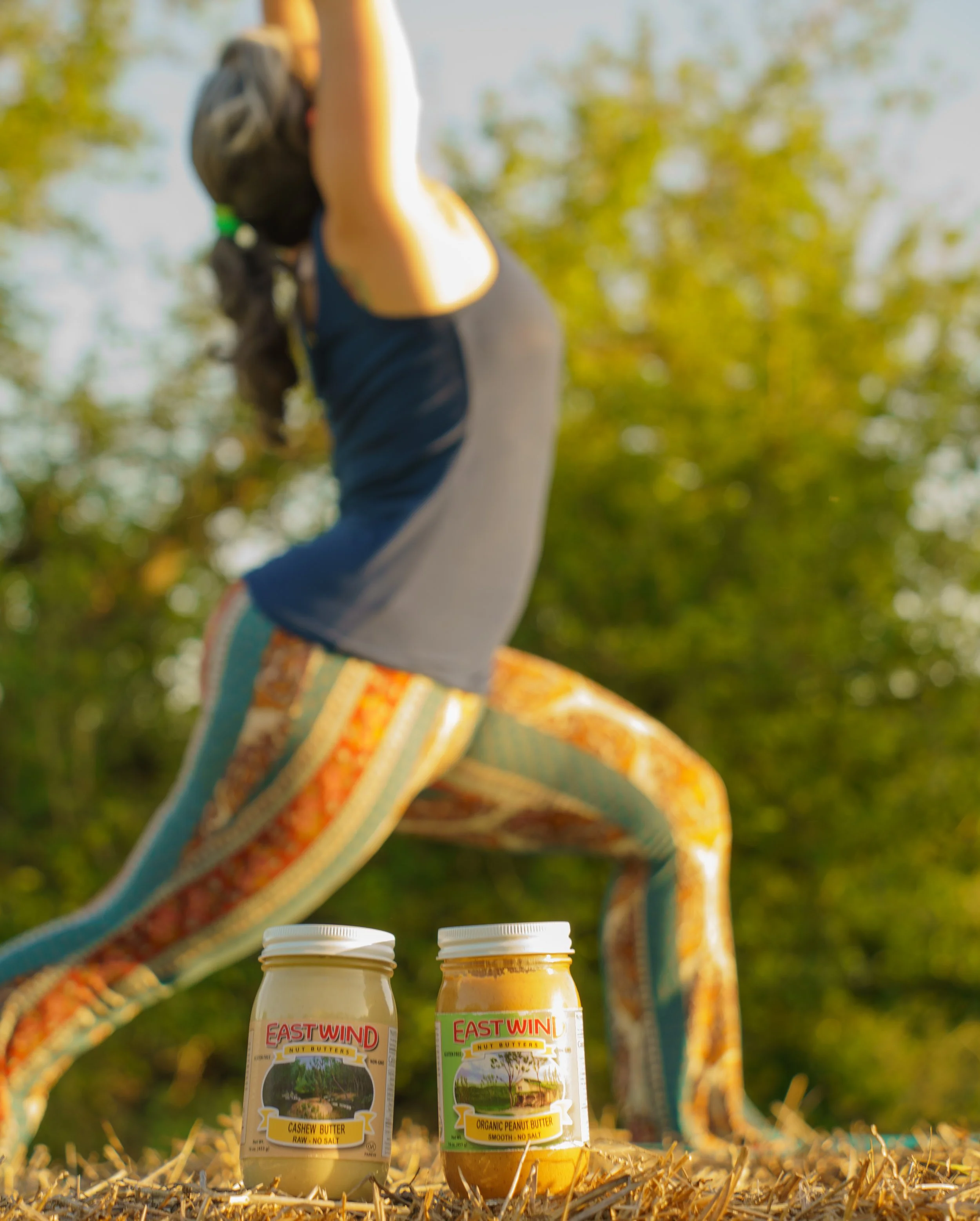 woman doing a yoga pose behind two 16oz jars of east wind nut butters