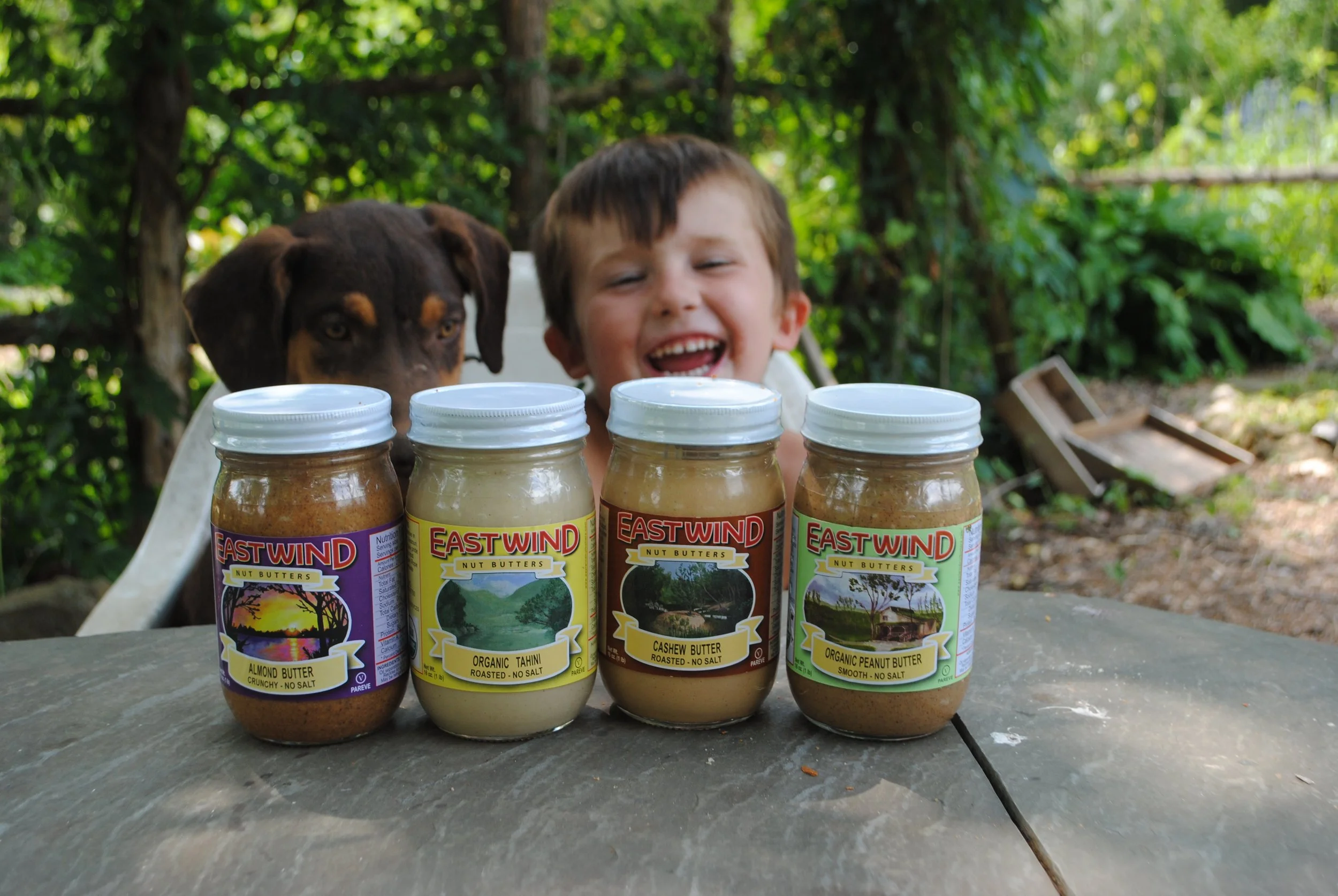 sampling of East Wind Nut Butters product line in front of a puppy and a young boy at a table