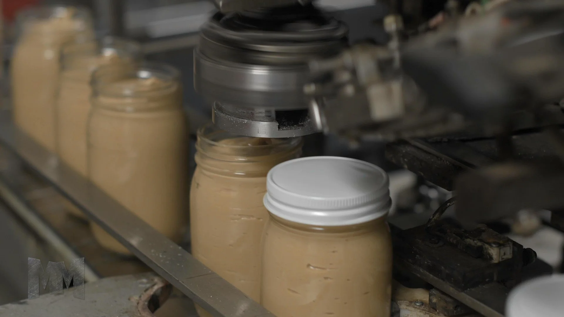 glass jars filled with organic valencia peanut butter being capped with a capping machine in a nut butter factory