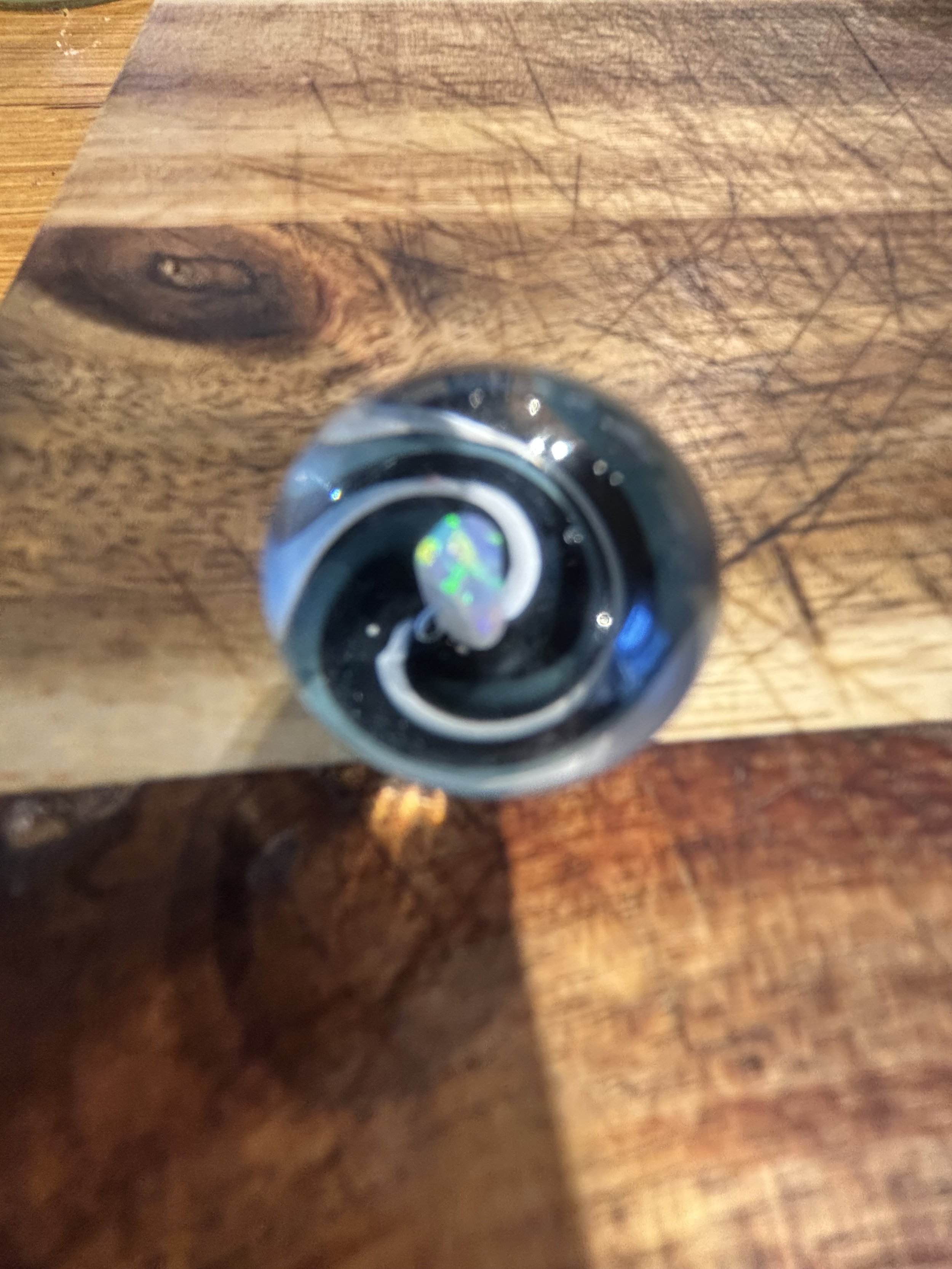 Glass marble on a wooden surface reflecting a rainbow-colored design inside.