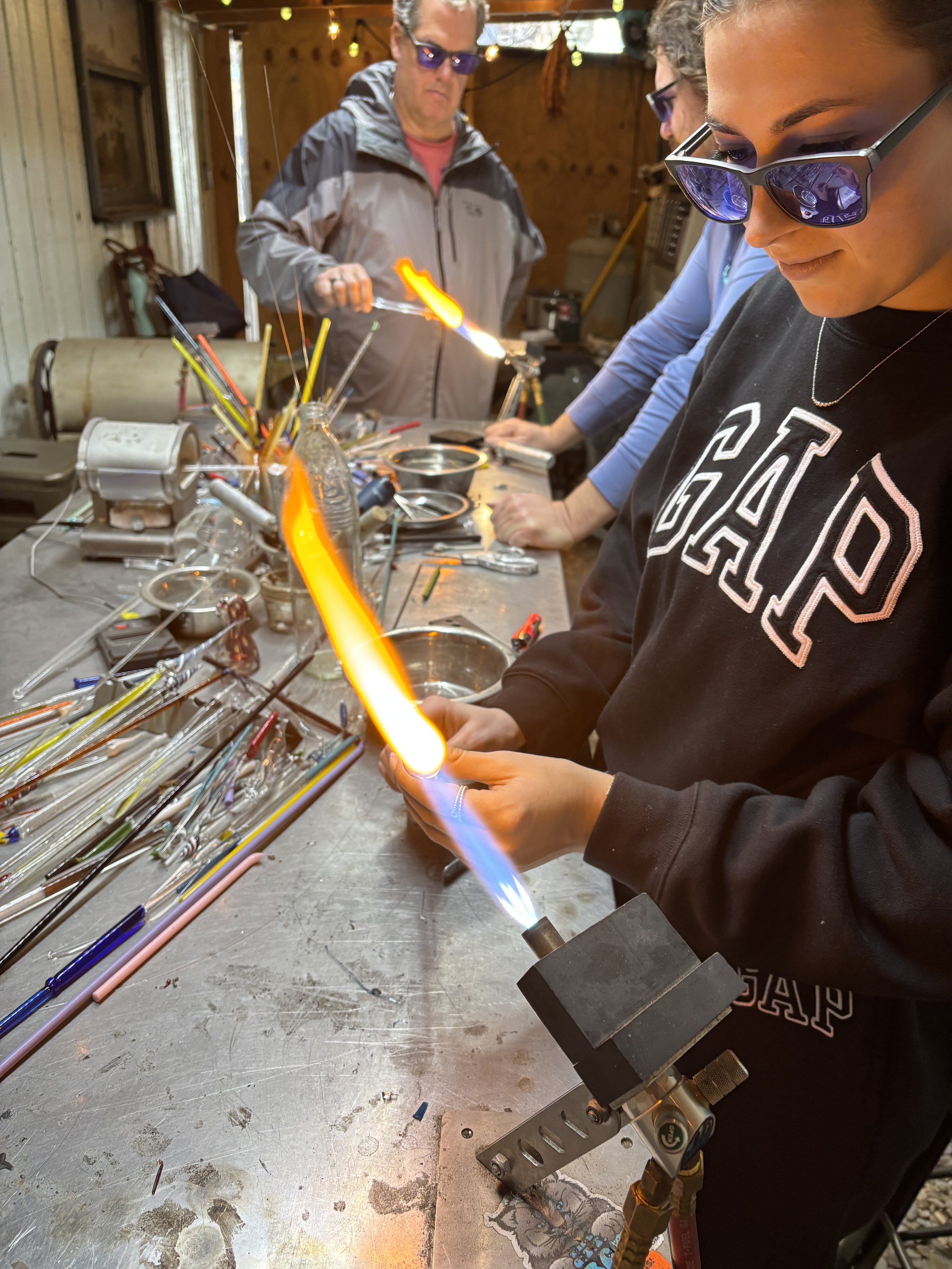 People working with glass blowing tools and colorful glass rods on a worktable in a workshop
