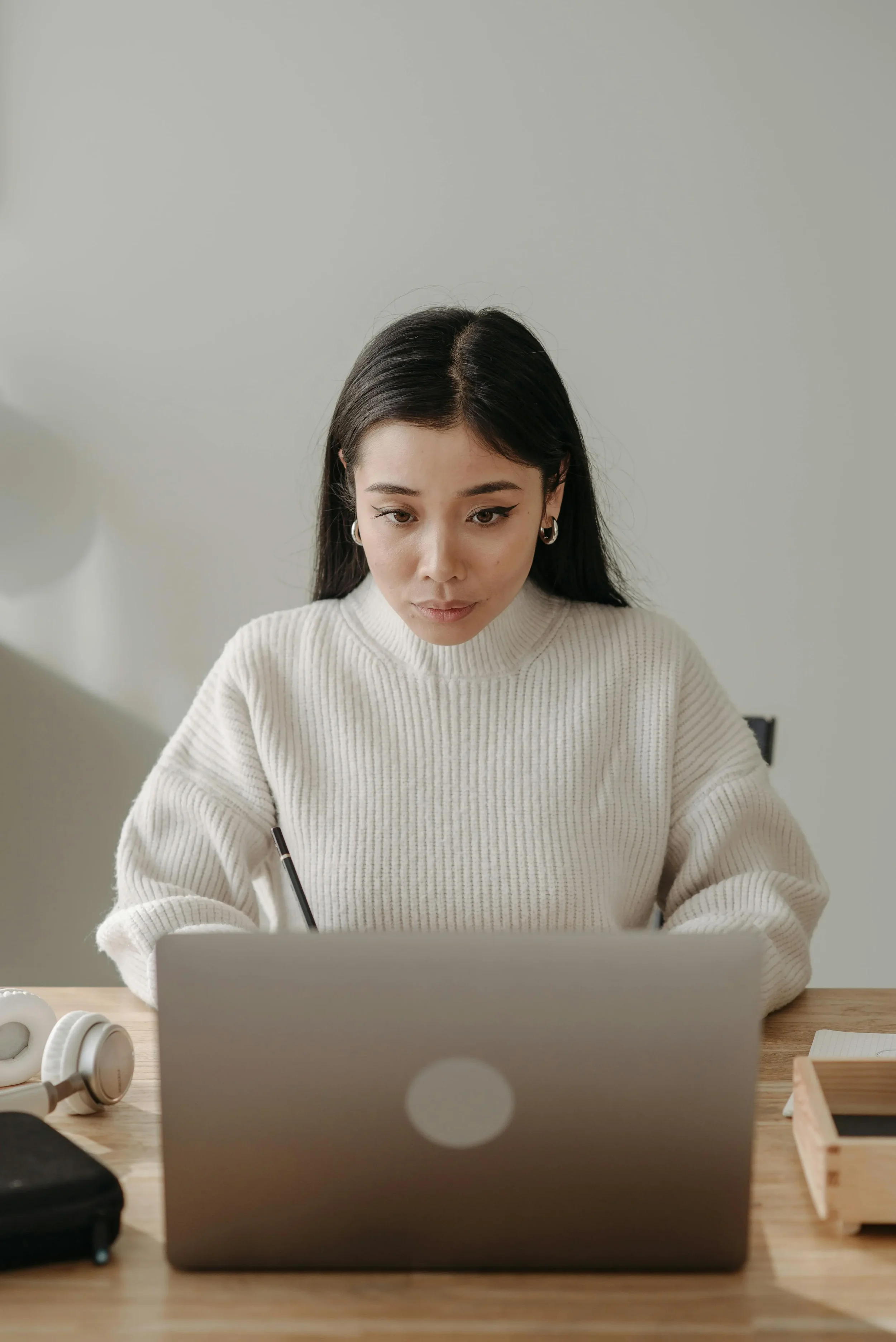 Woman concentrating while working on a laptop with headphones nearby, representing focus and potential mental fatigue