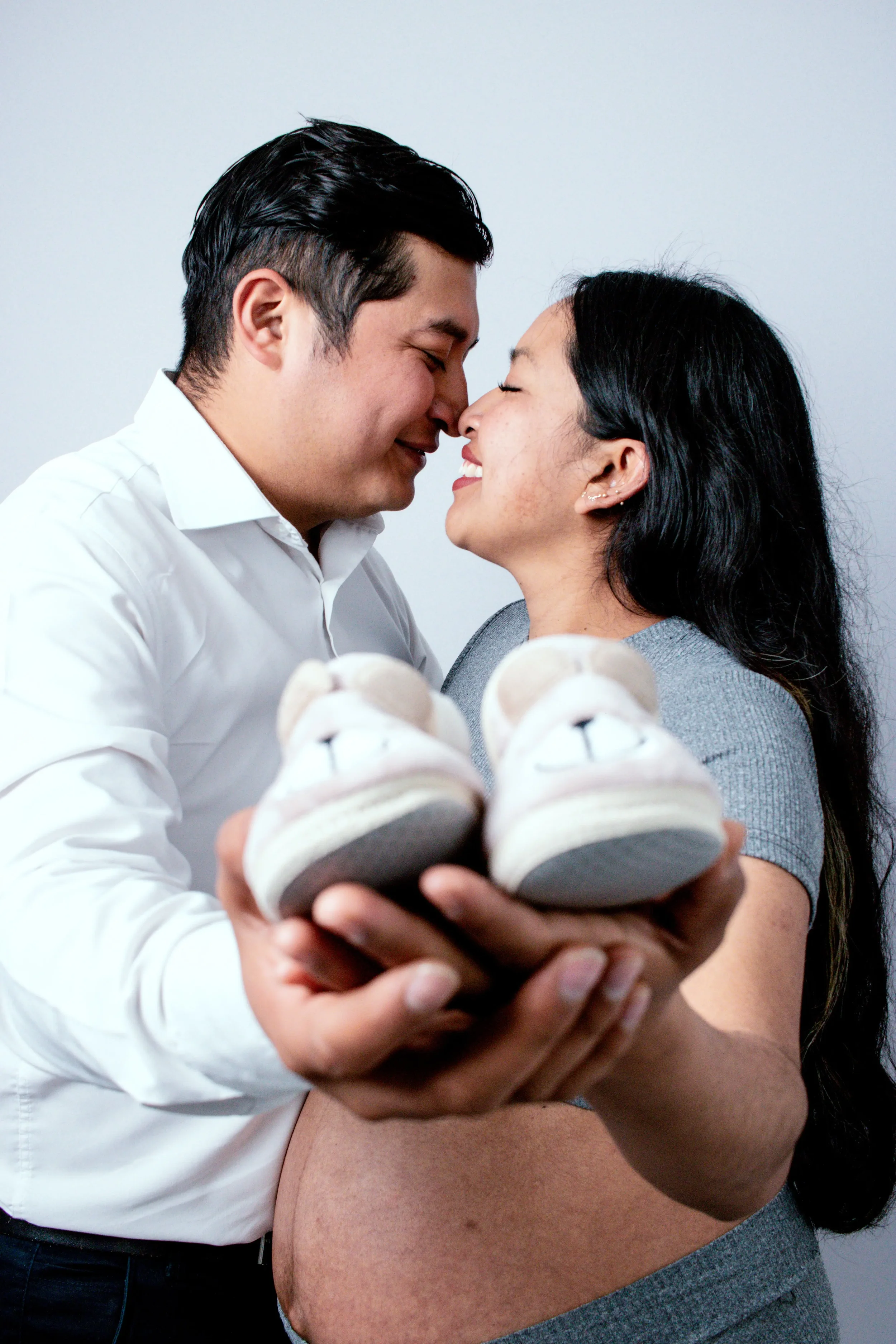 Expecting couple holding baby shoes and smiling at each other while preparing for the transition to parenthood together.
