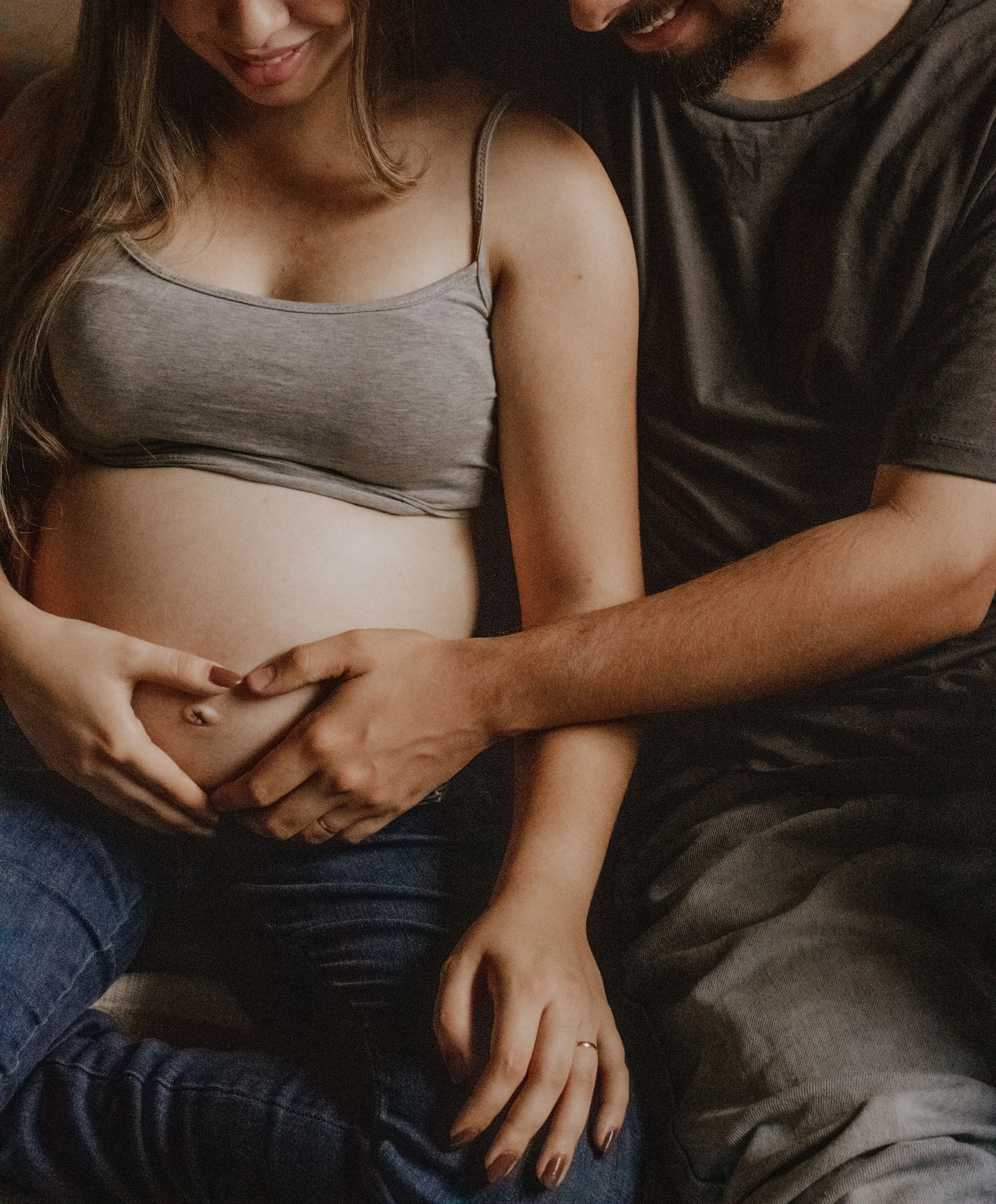 Couple gently holding a baby bump together, symbolizing teamwork and connection while preparing to welcome a child.