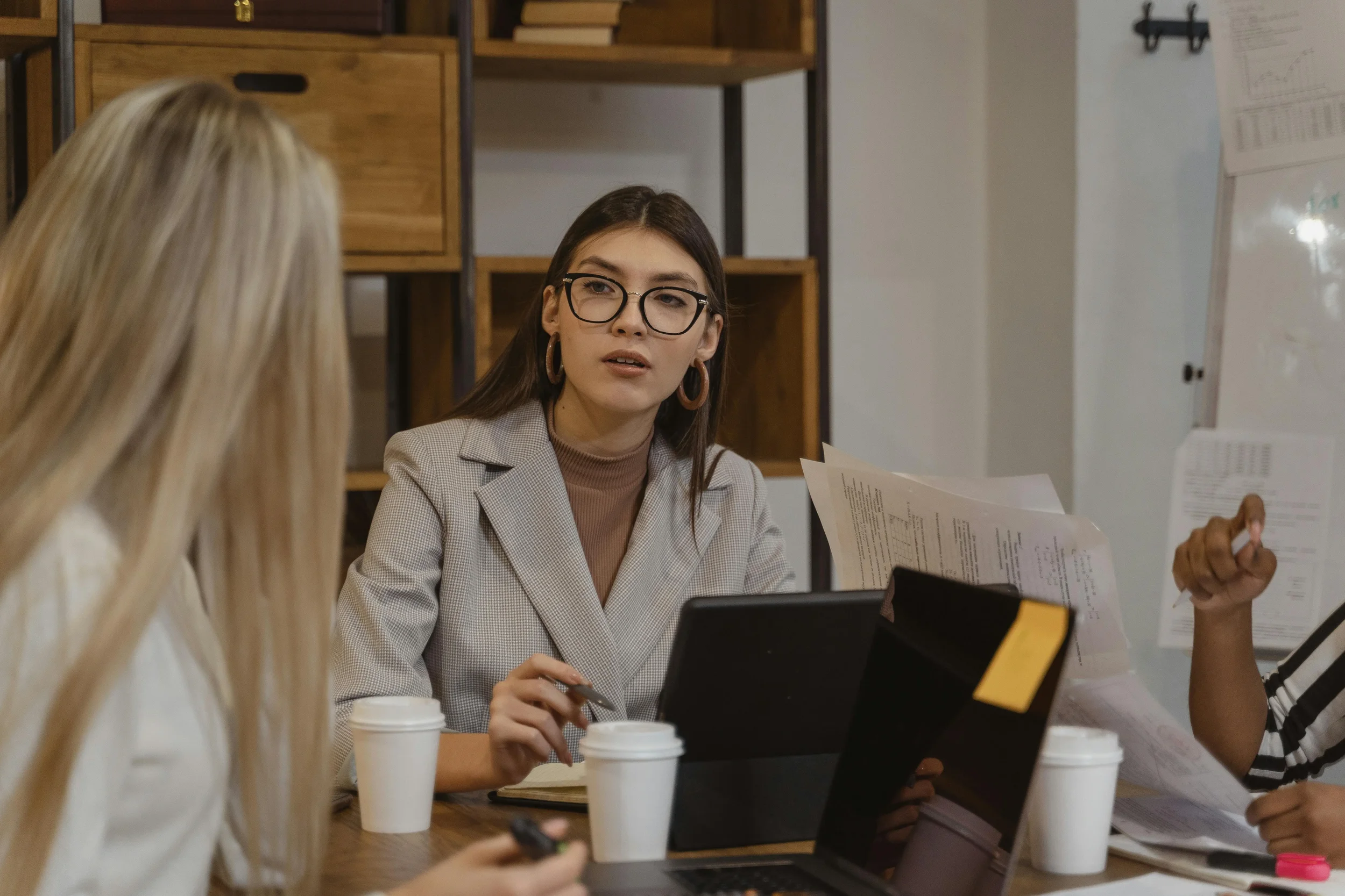 Woman speaking and holding papers during a discussion with others, suggesting a work meeting or consultation setting