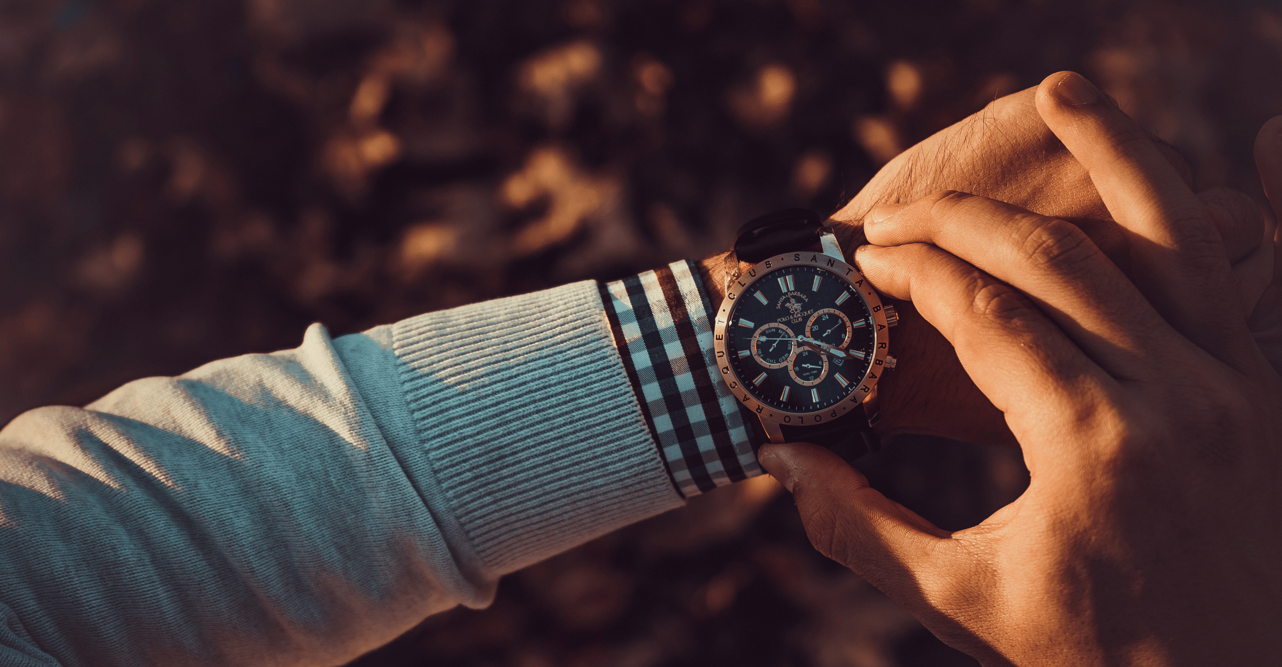 Close up of an arm showing a wristwatch. Another hand is adjusting the dial.