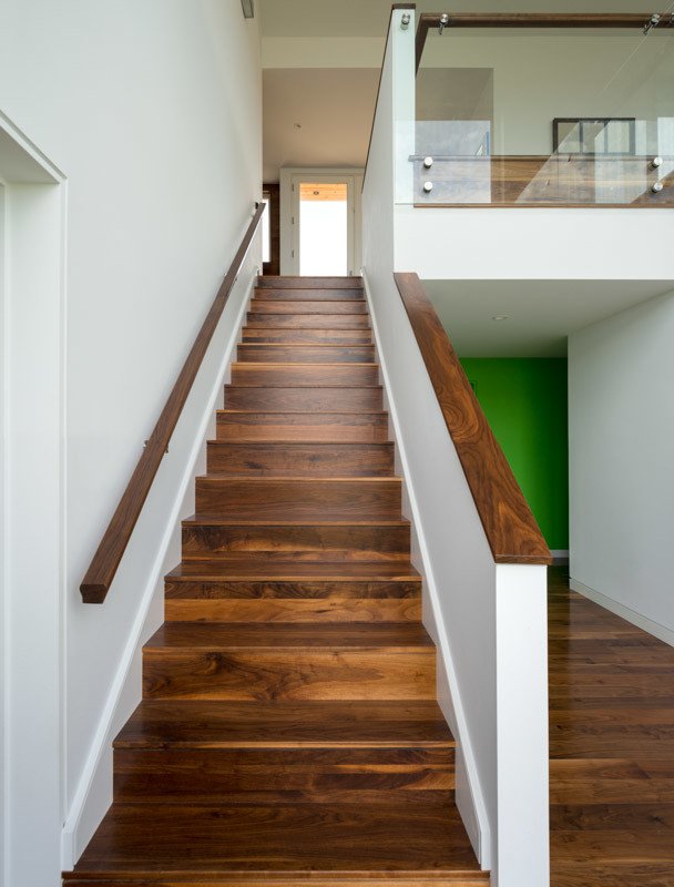 Interior with wooden stairs and railing leading to an upper floor, white walls, green accent wall, and glass balcony.