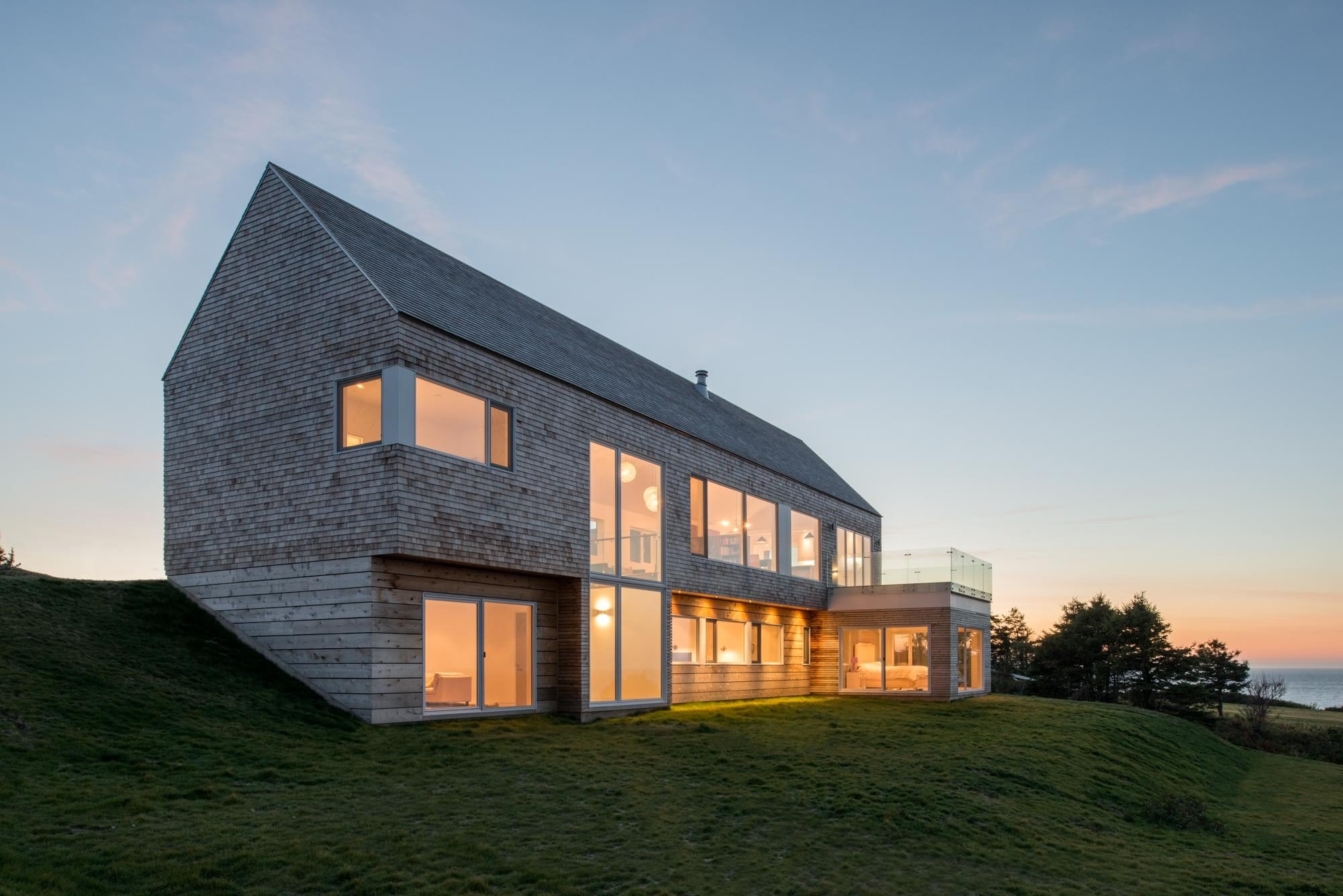 Modern house with large windows on a grassy hill at sunset.