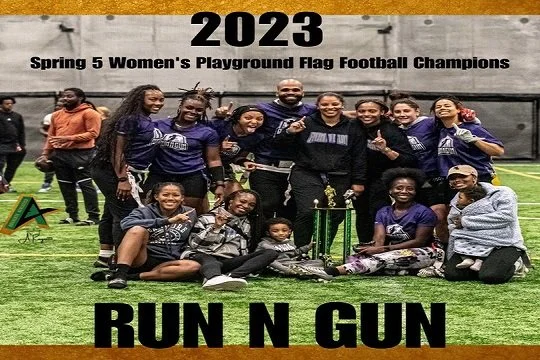 Group of women and children on a football field celebrating their victory as 2023 Spring 5 Women's Playground Flag Football Champions, with a trophy and banner reading 'RUN N GUN'.