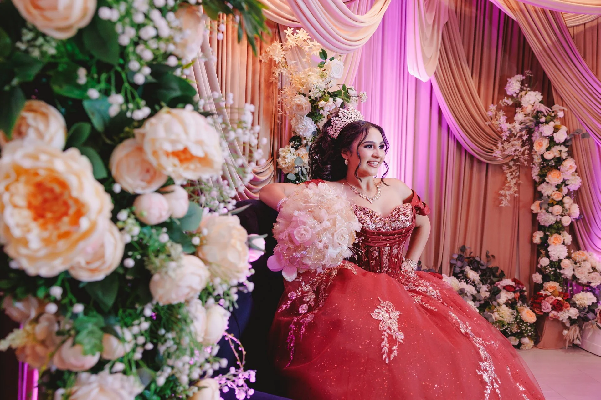 Quinceneara in a red gown posed with elegant flower decorations