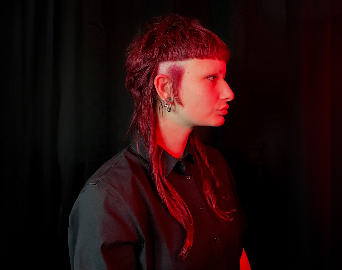 Profile photo of a young woman with red hair and red lighting on a black background.