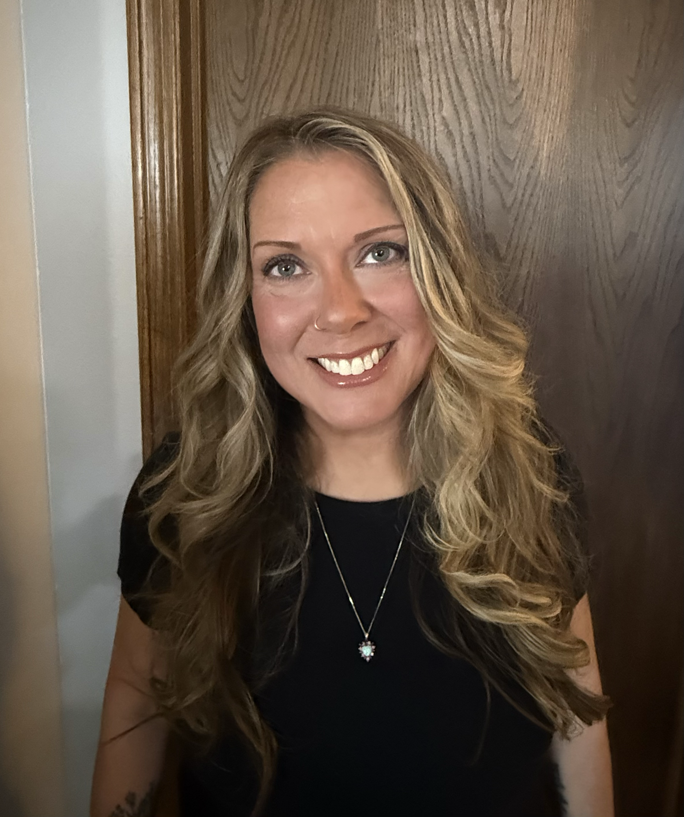 A woman with shoulder-length wavy blonde hair smiling, wearing a navy blazer and a light-colored blouse against a neutral background.